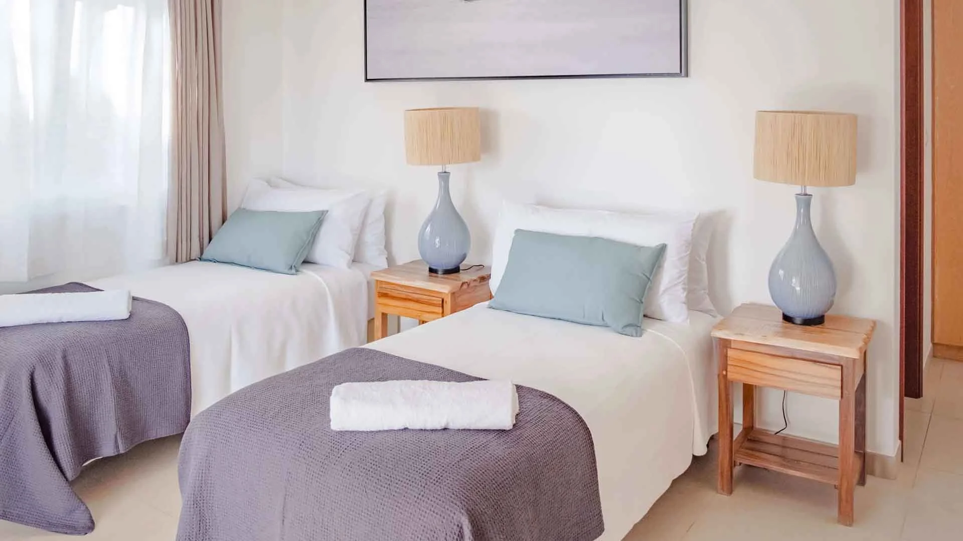 Guest bedroom at Farquhar Lodge, Seychelles, featuring two beds, side tables with lamps, and a painting on the wall.
