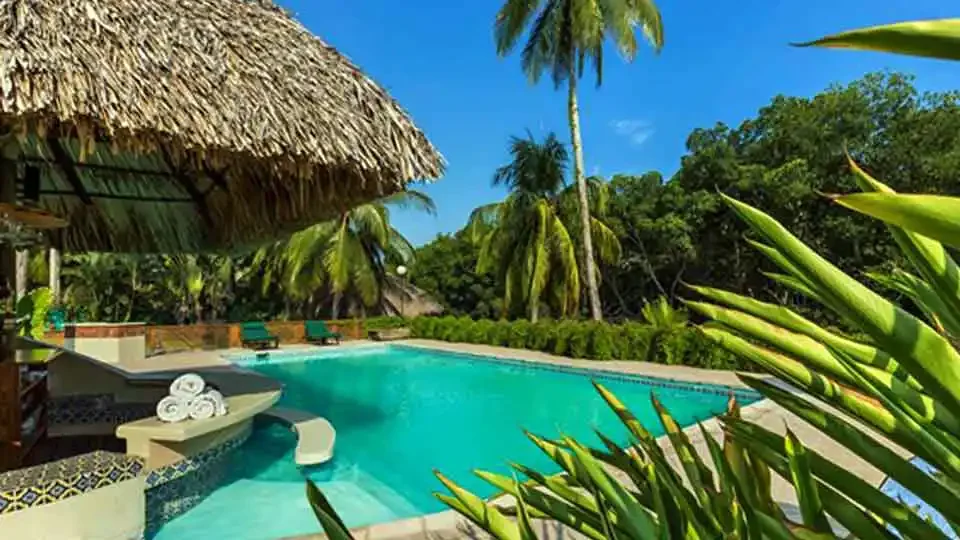 Beautiful swimming pool with swim-up bar surrounded by palm trees at Sailfish Oasis Lodge in Guatemala.