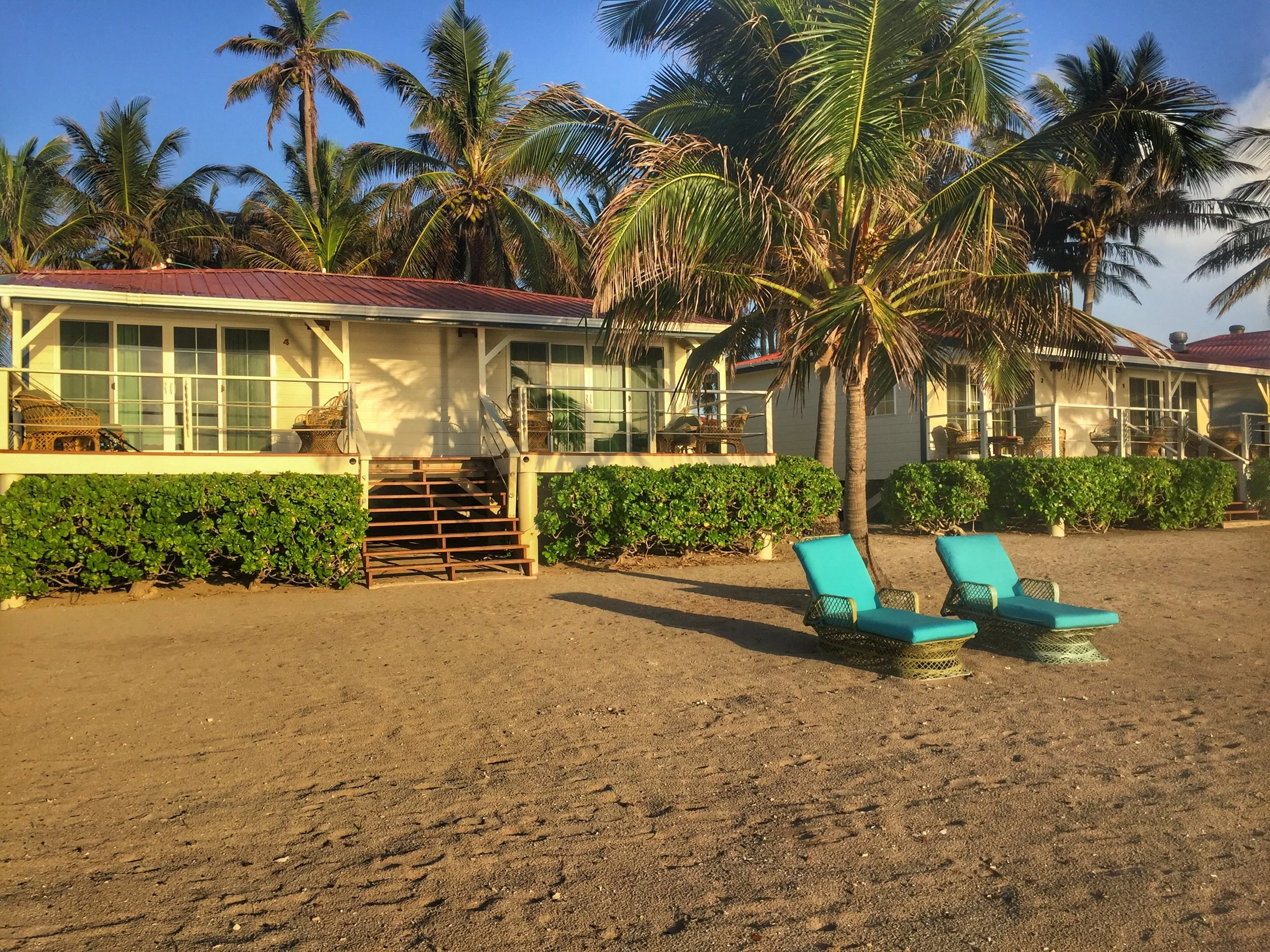 Beachfront cabanas at Turneffe Atoll with two lounge chairs on the sand