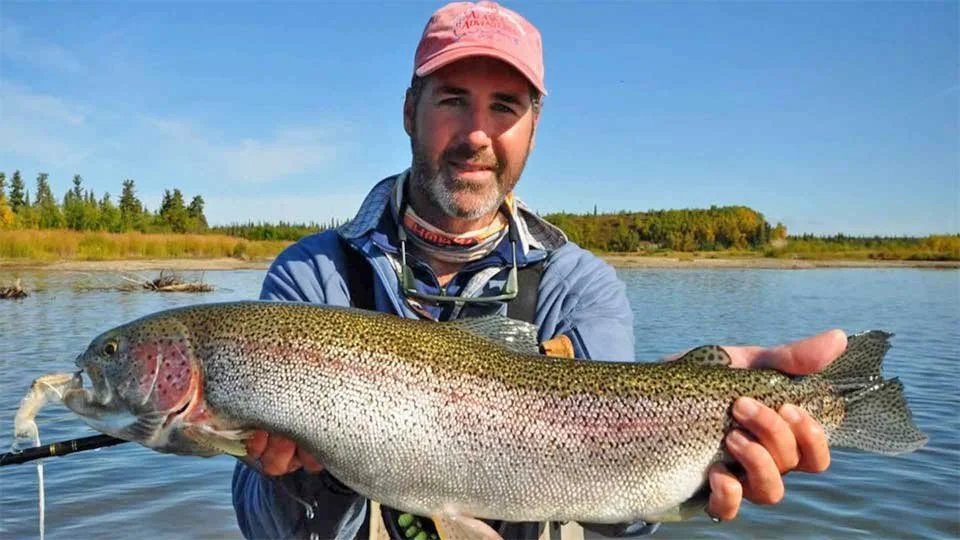 Angler holding a large rainbow trout at an Alaska fishing lodge, ready for release