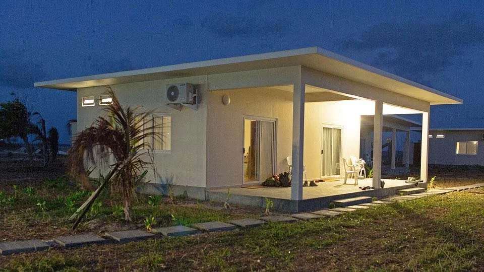 Nighttime view of a Farquhar Lodge chalet in Seychelles, with a light on the front porch, surrounded by green grass and small palm trees.