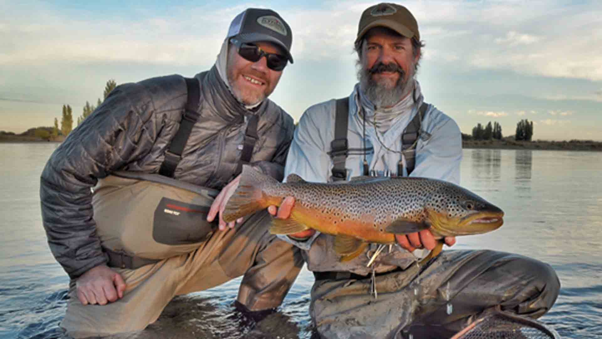 “Angler and guide holding a beautifully colored brown trout on the Limay River in Patagonia during a guided fly fishing trip.”