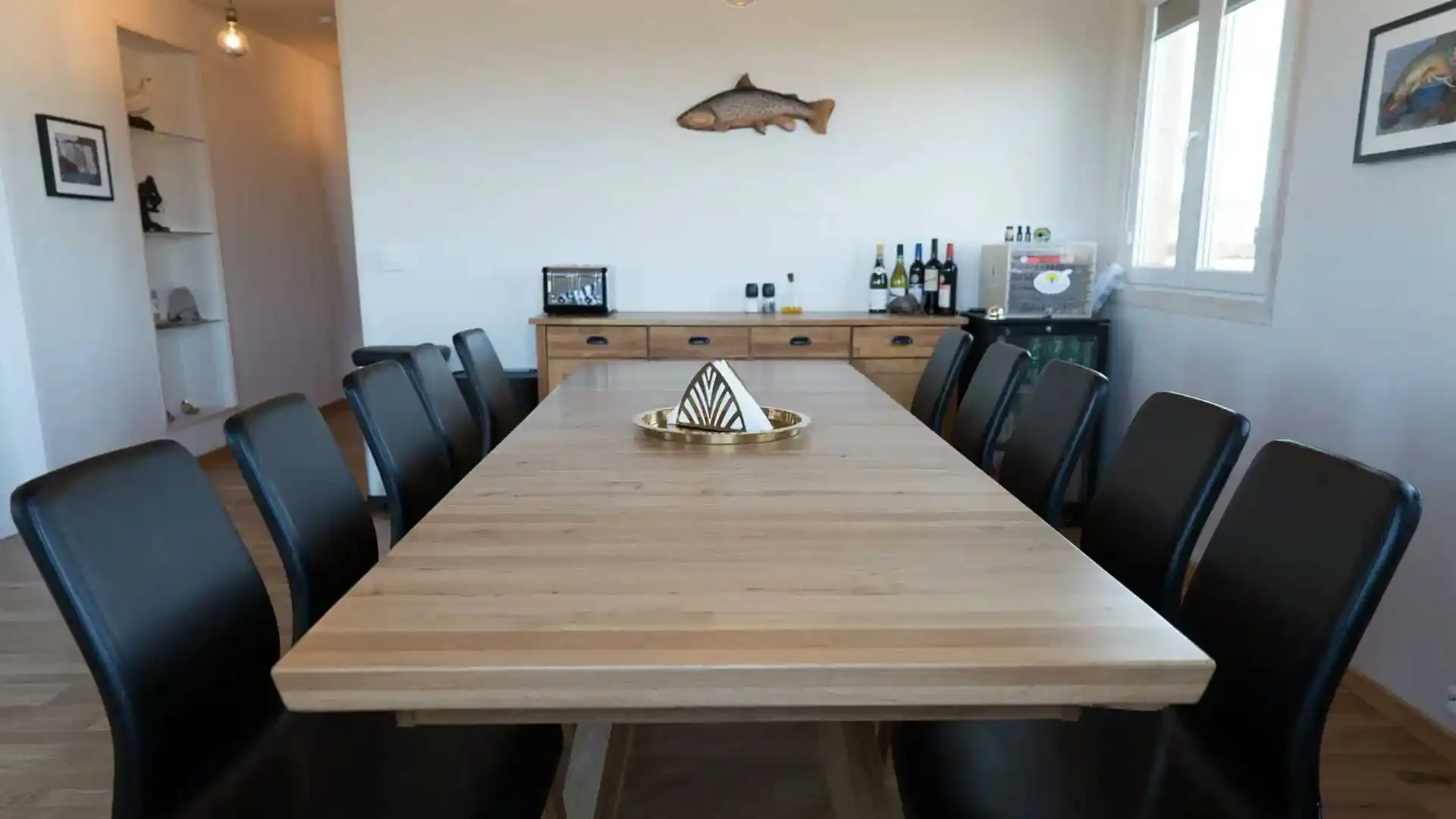 Spacious dining room in an Icelandic Highland fishing lodge with a long wooden table, black chairs, and a fish decoration.