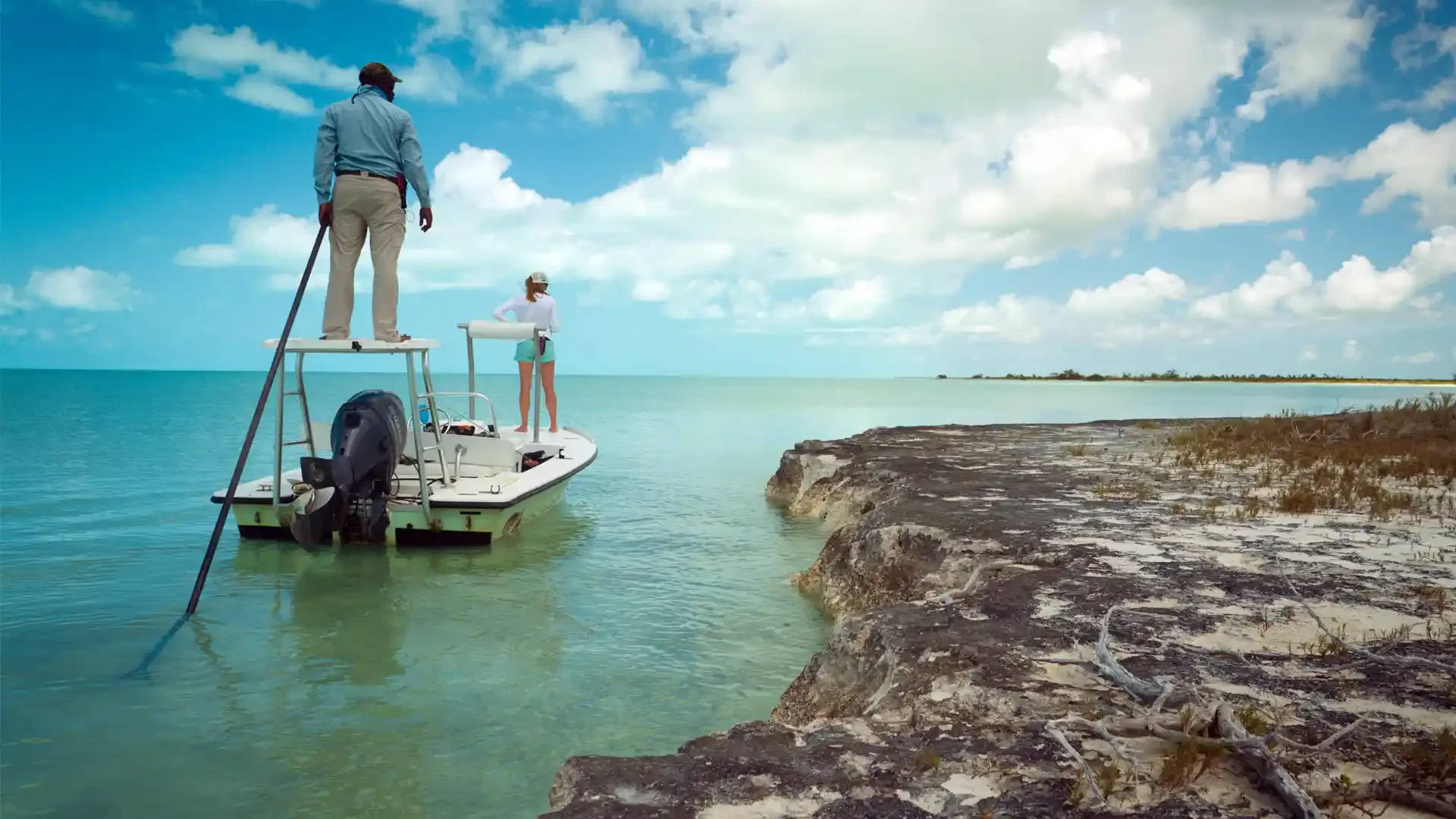 People on a boat near a rocky shore with a clear sky and scattered clouds.
