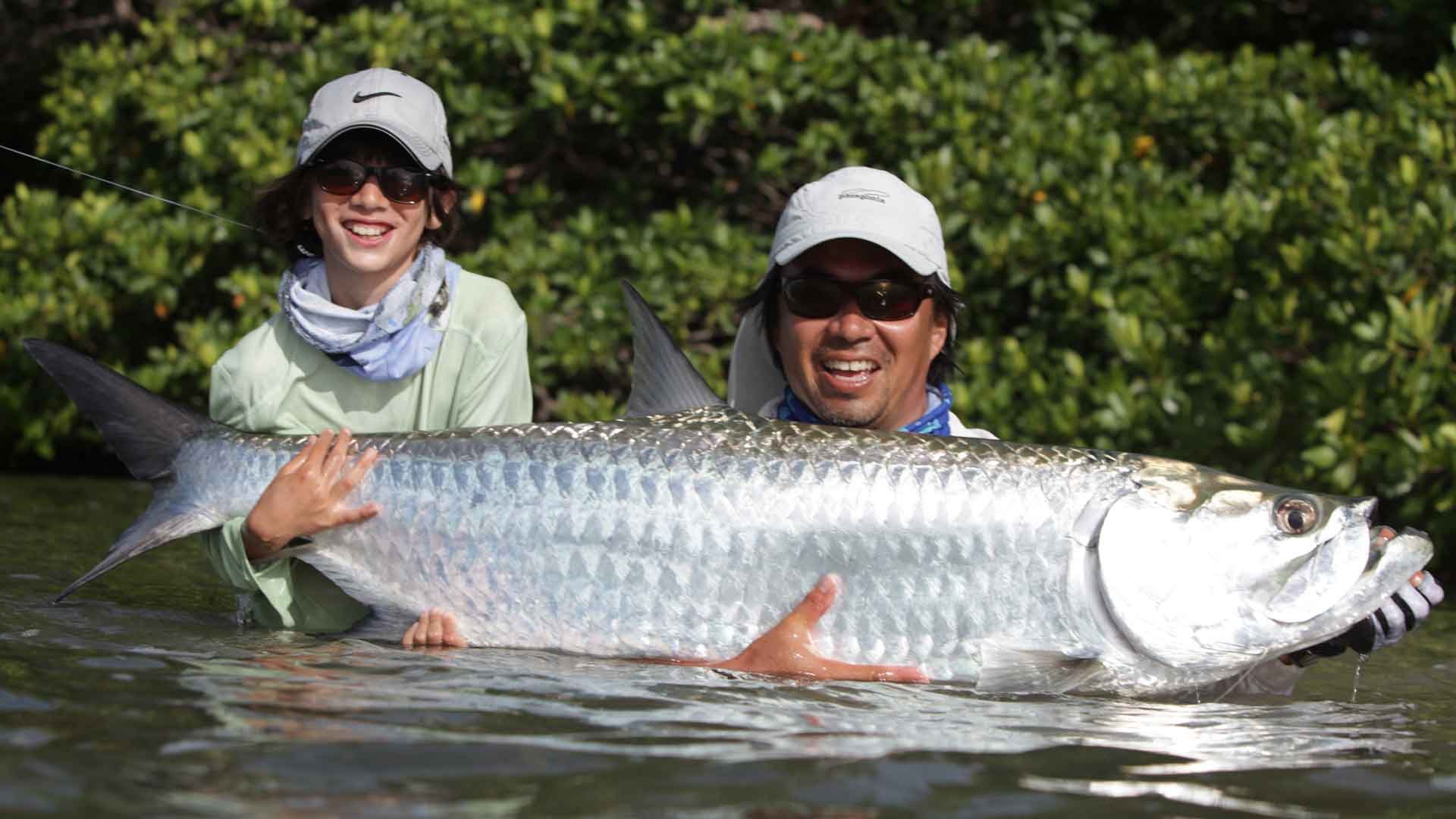 El Pescador Lodge guide helping a young angler hold a tarpon in the water on the flats of Ambergris Caye, Belize.
