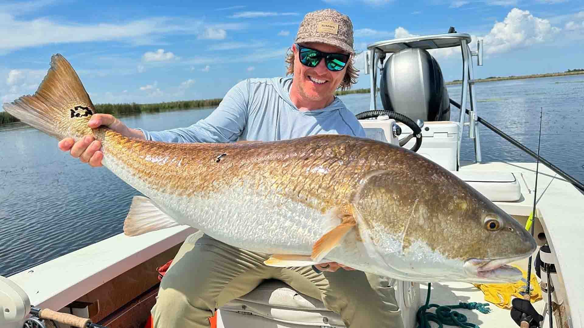 Smiling angler proudly displays a massive redfish caught fly fishing in the Louisiana marsh from a boat.
