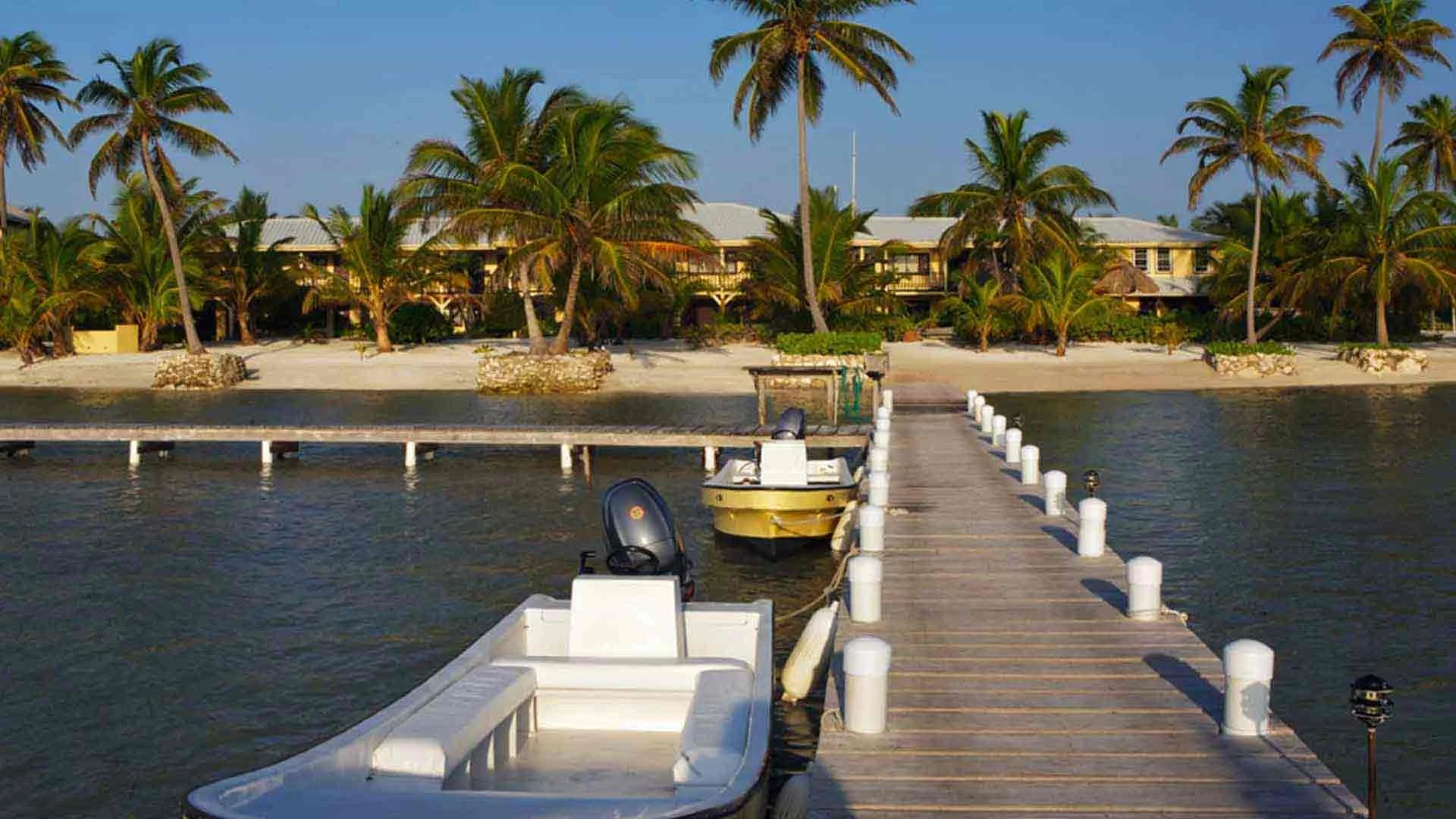 Two 23-foot saltwater flats fishing boats tied to the dock in front of El Pescador Lodge on Ambergris Caye, Belize, ready for anglers.