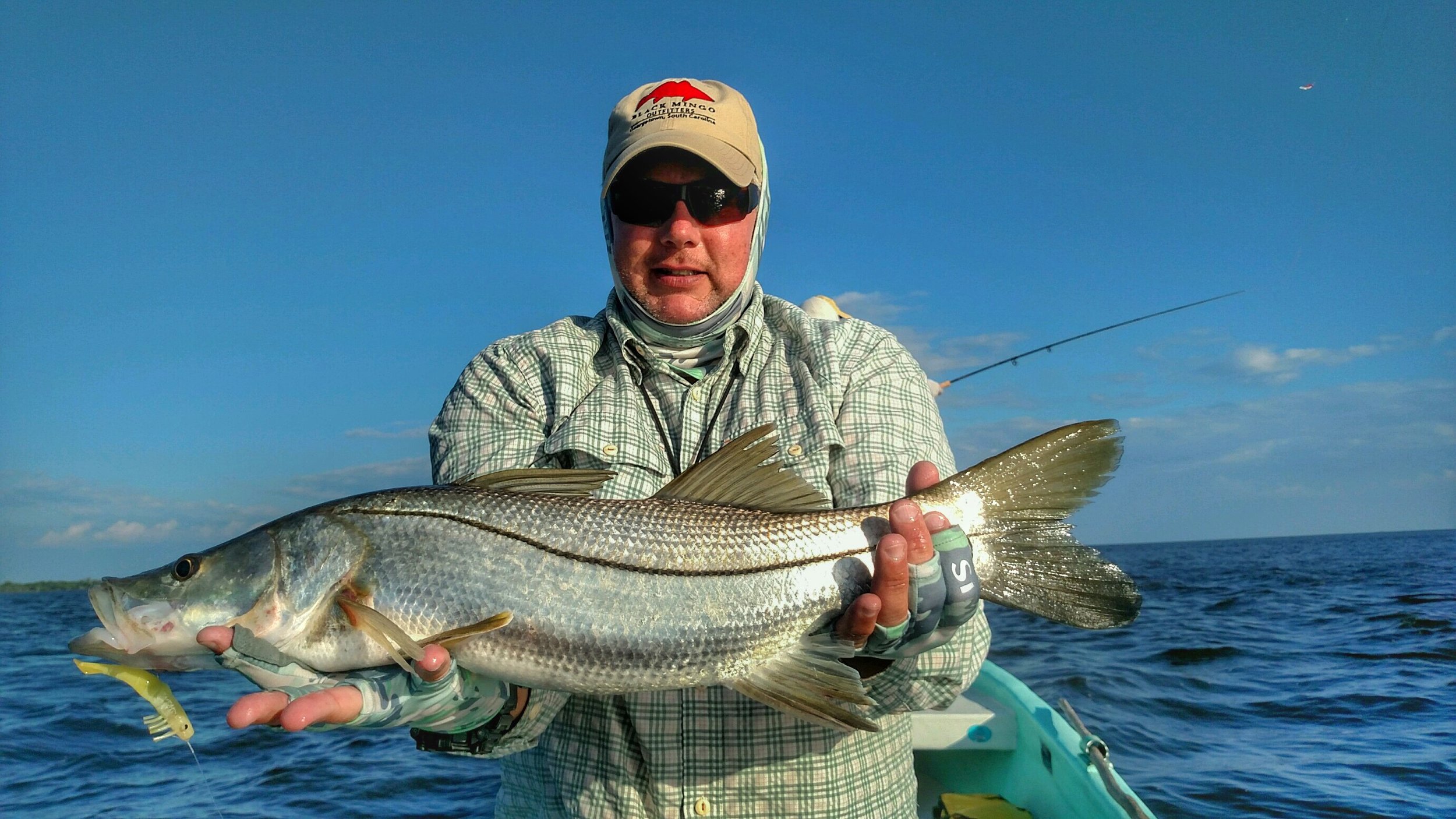 Angler holding a large snook caught while fishing near Belize River Lodge, Belize, with clear blue skies and choppy water.
