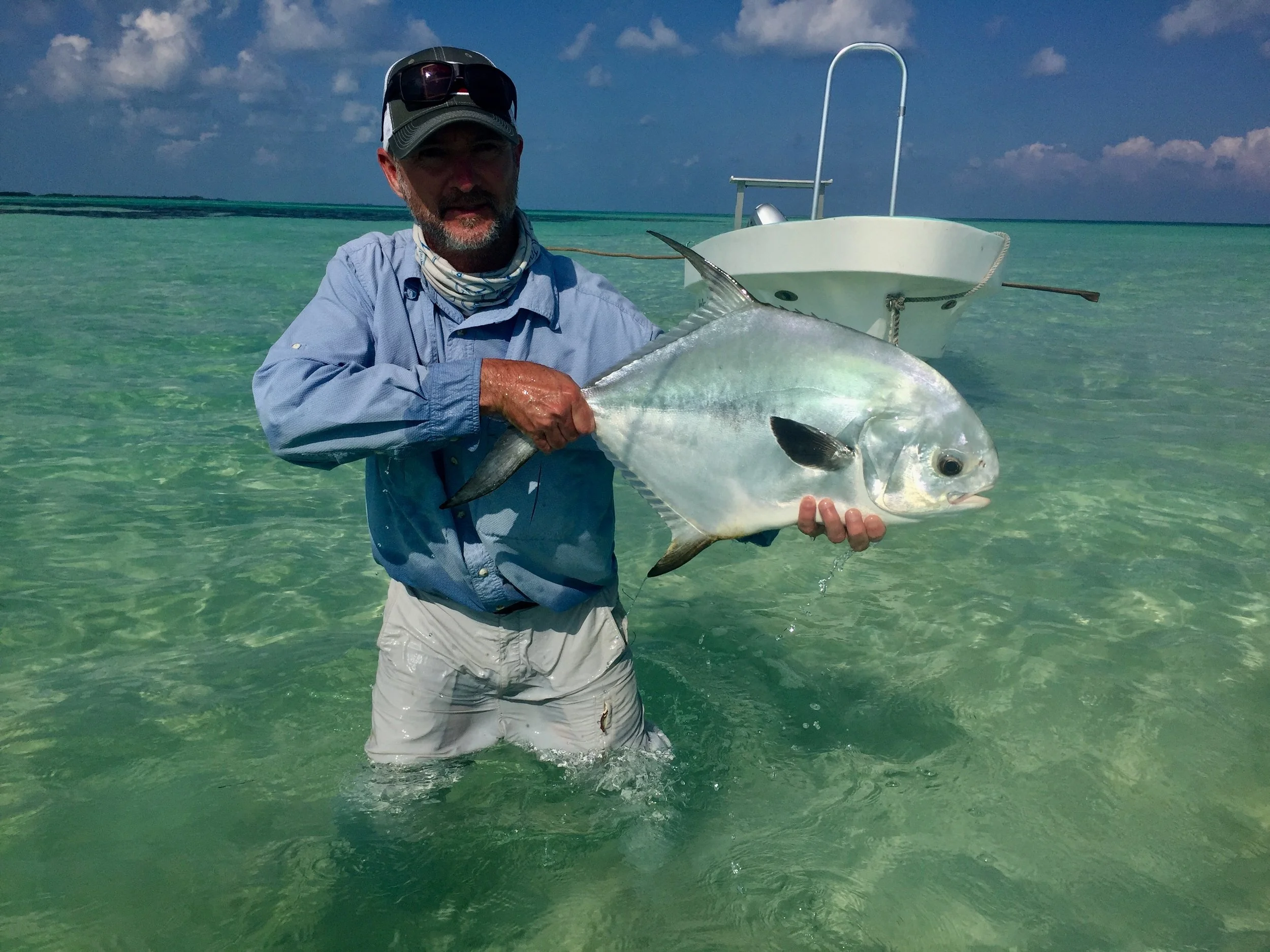 Angler holding a large permit fish in the clear saltwater flats of Belize, with a skiff in the background.