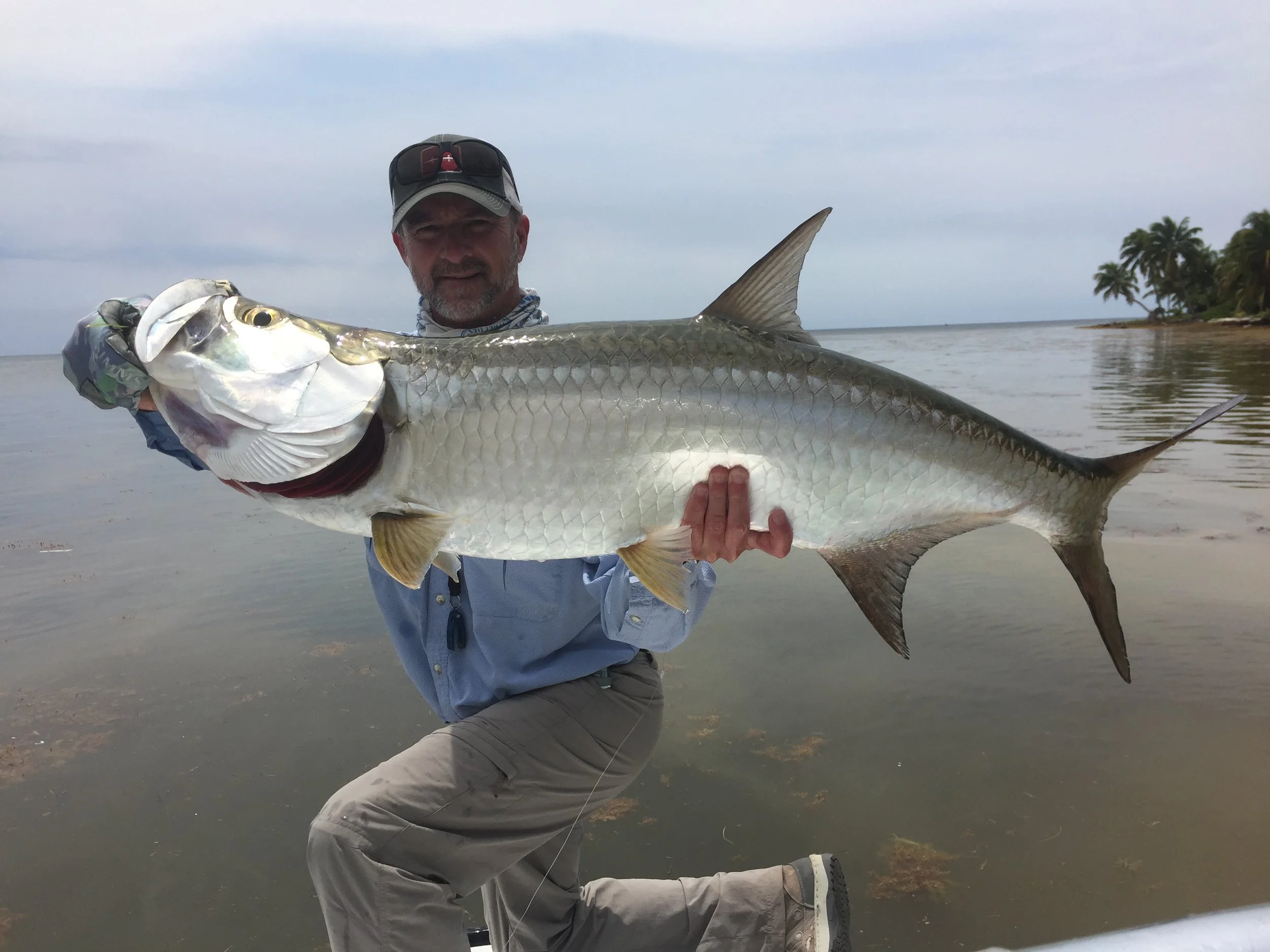 Angler holding a large shiny tarpon with calm Caribbean waters at Turneffe Flats Resort in the background
