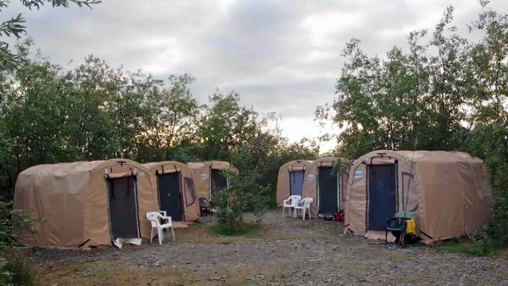 Dave Duncan & Sons fly fishing camp in Alaska with multiple tan canvas tents nestled among green trees under an overcast sky.