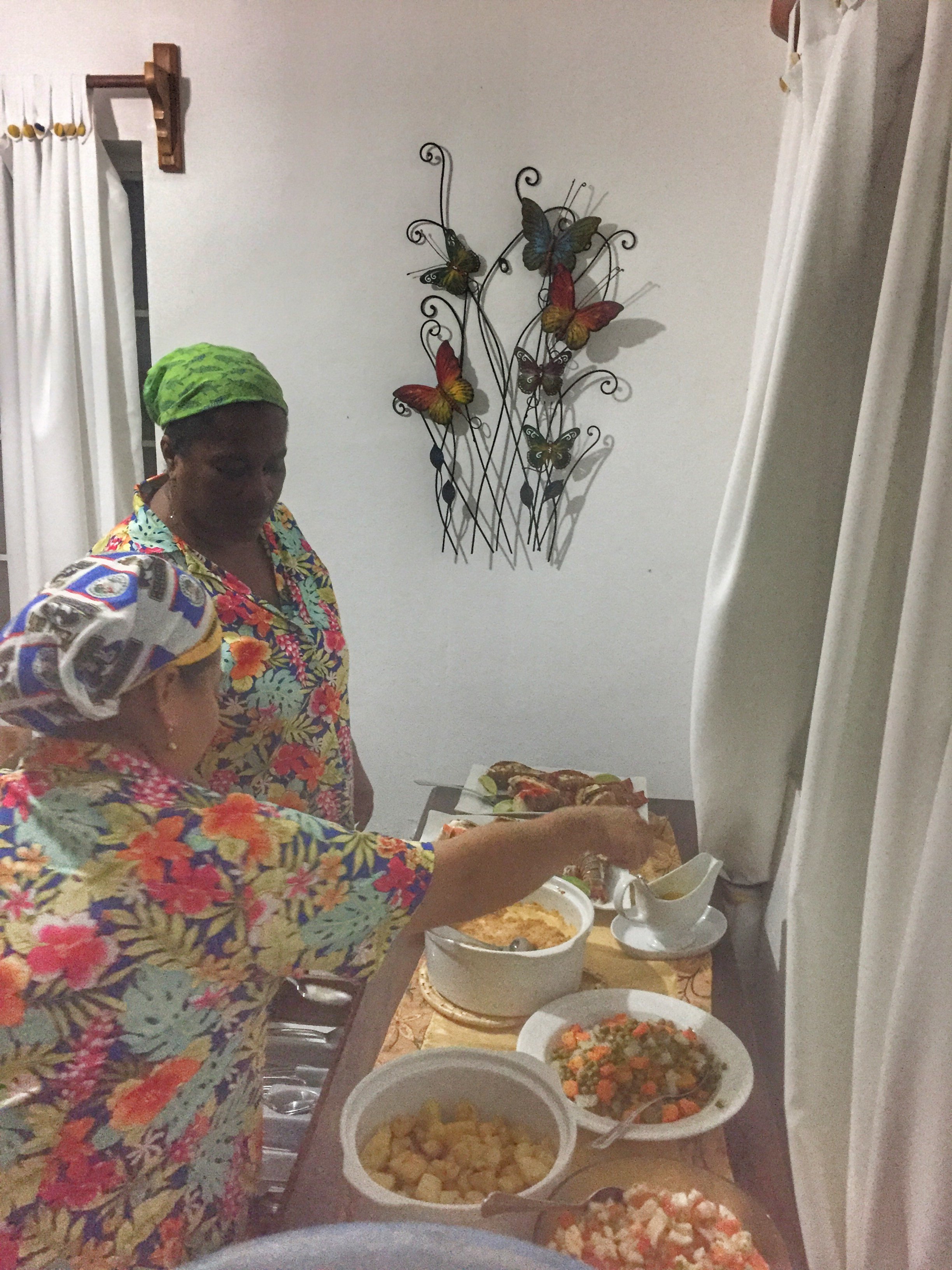 Two women in floral attire serving local dishes at Belize River Lodge, highlighting Belizean hospitality.