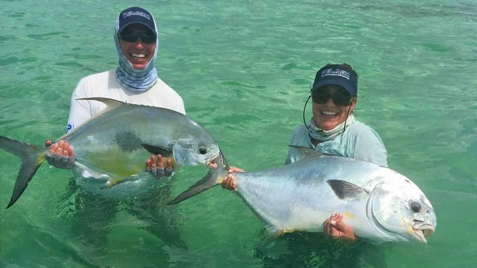 Two happy anglers holding large permit in the clear shallow flats of Ambergris Caye, Belize, after a successful day of fishing.