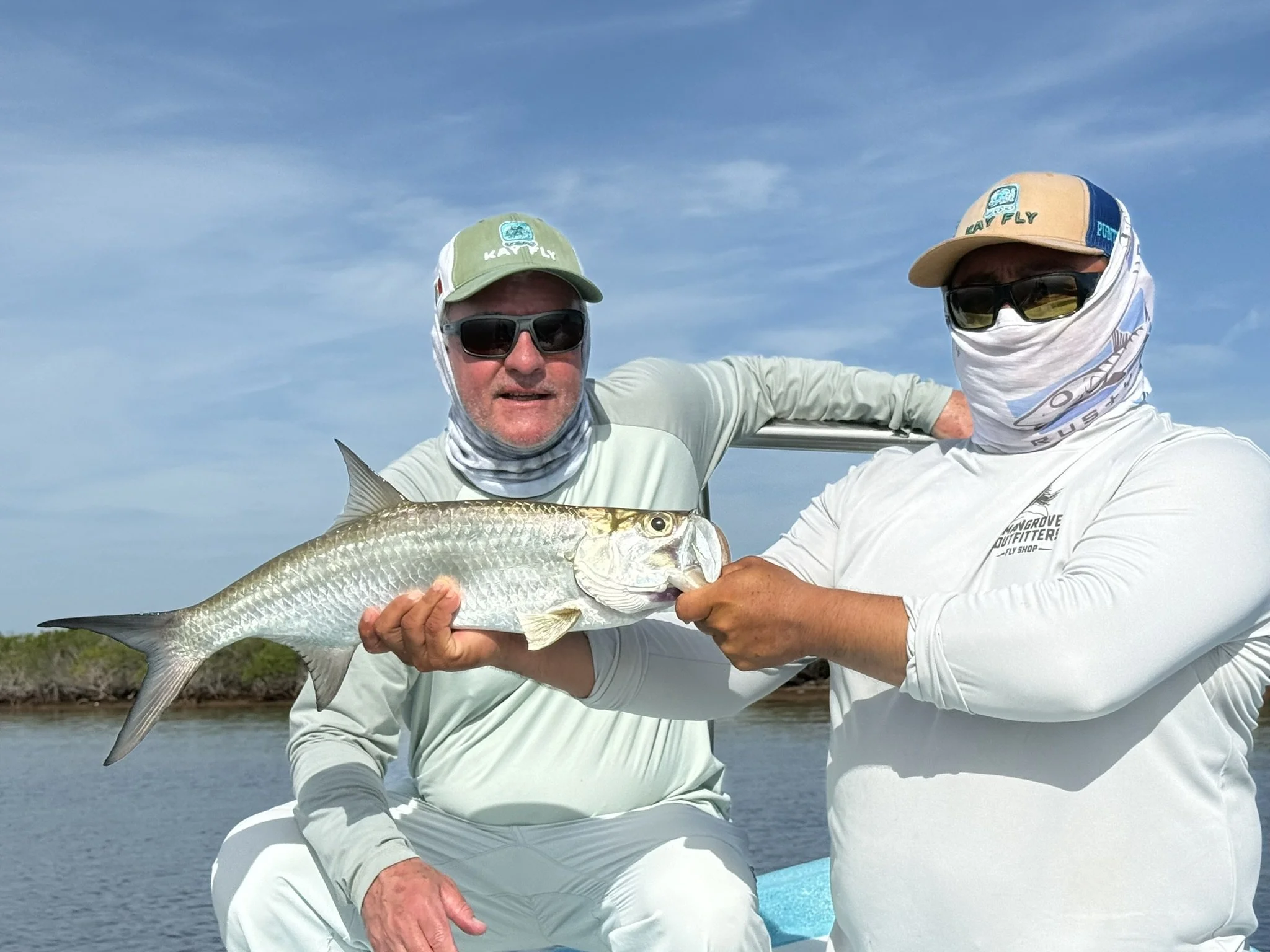 Kay Fly Lodge fishing guide helping an angler display a tarpon on a boat, with water and sky in the background.
