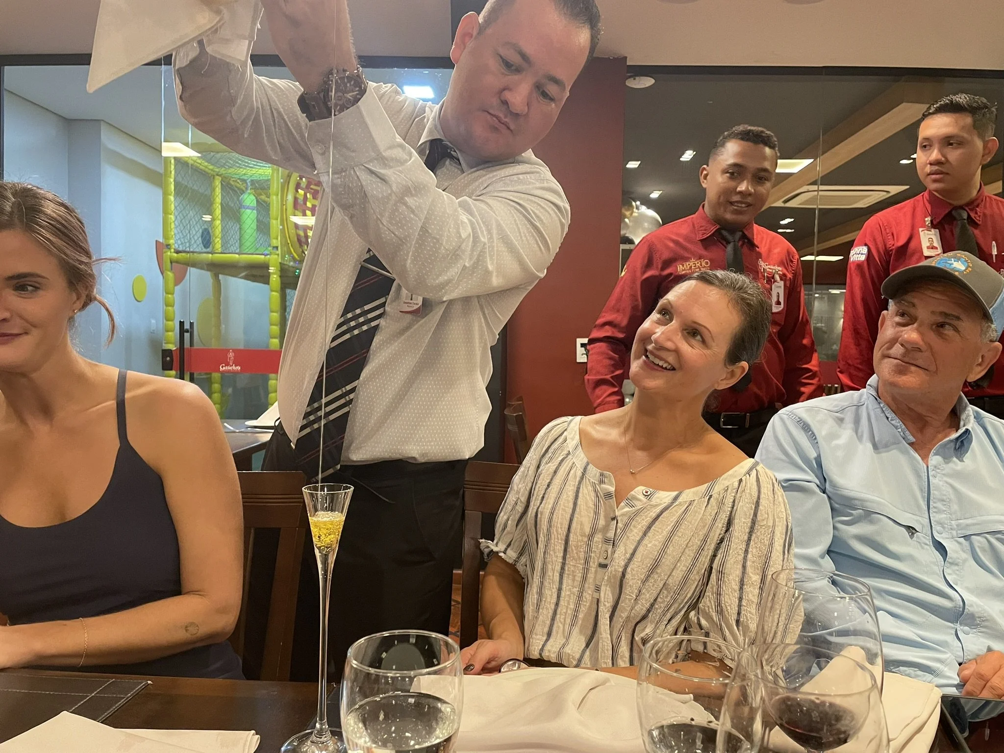 People celebrating at a restaurant, with a waitress pouring champagne.