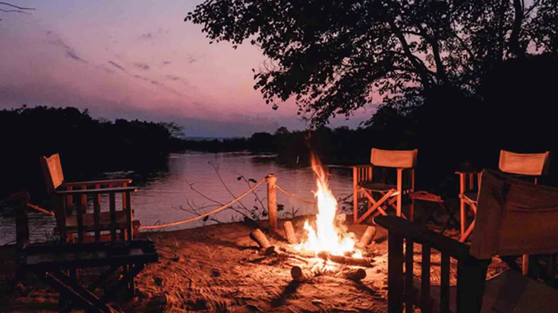 Campfire by a warmwater river at sunset in Tanzania, chairs set for a relaxing evening after a day of Tigerfish angling.