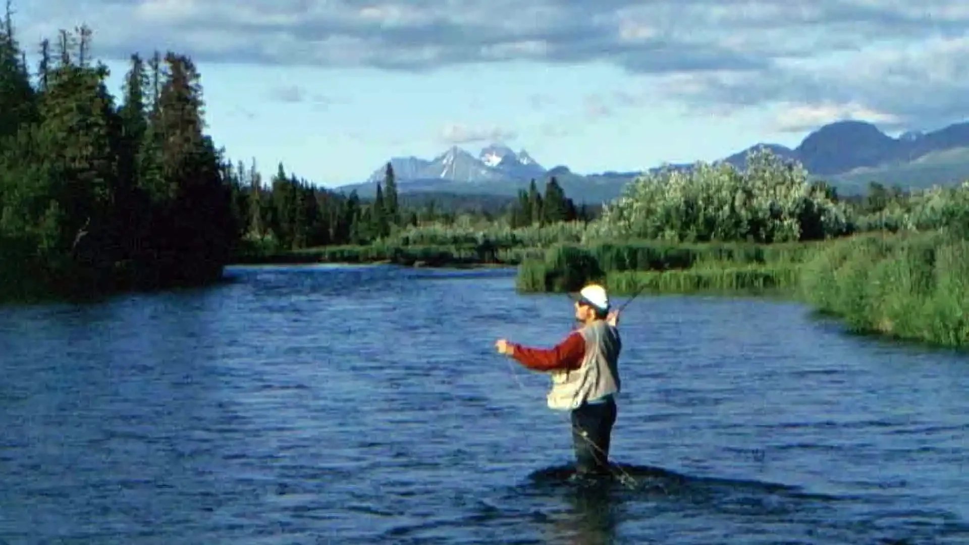 Angler standing on the Copper River in Alaska, casting for trout with the Copper Mountains in the distance during a guided fly fishing trip from Copper River Lodge.