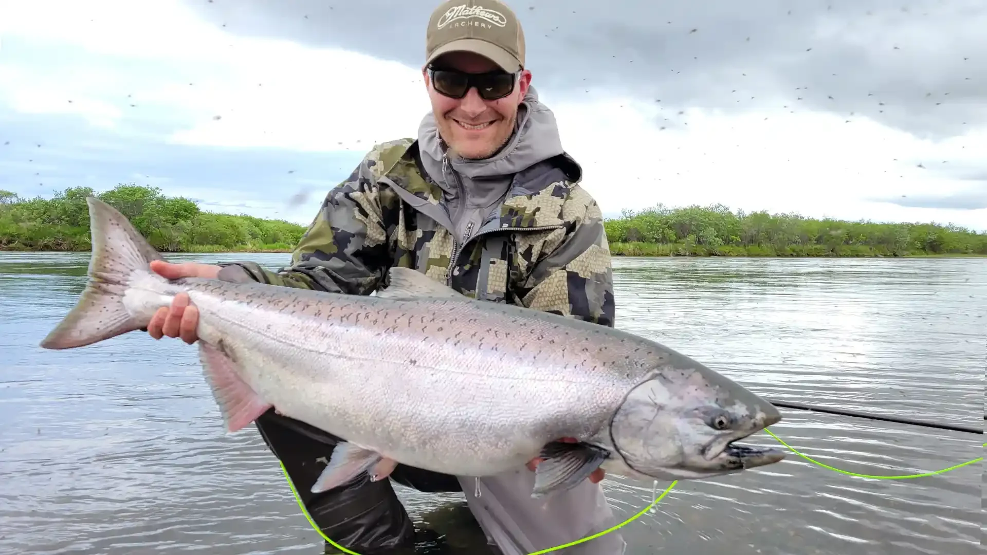 Happy angler holding a large King Salmon in an Alaskan river, surrounded by insects, with Dave Duncan & Sons.