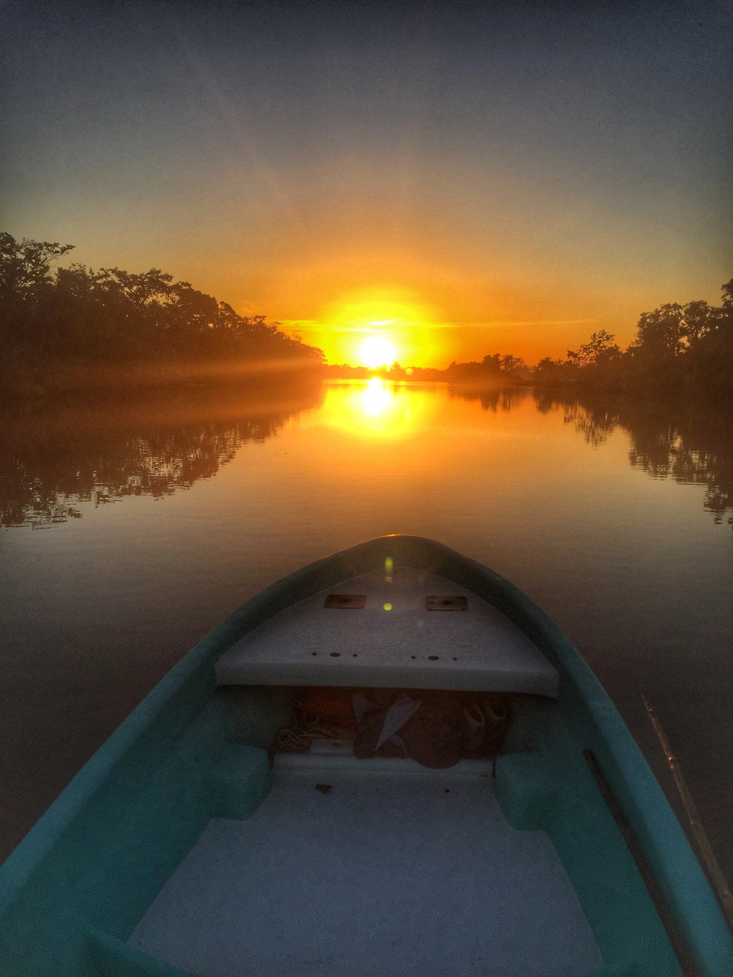 Early morning fly fishing on the Belize River from a boat, with a vibrant sunrise over Belize River Lodge.