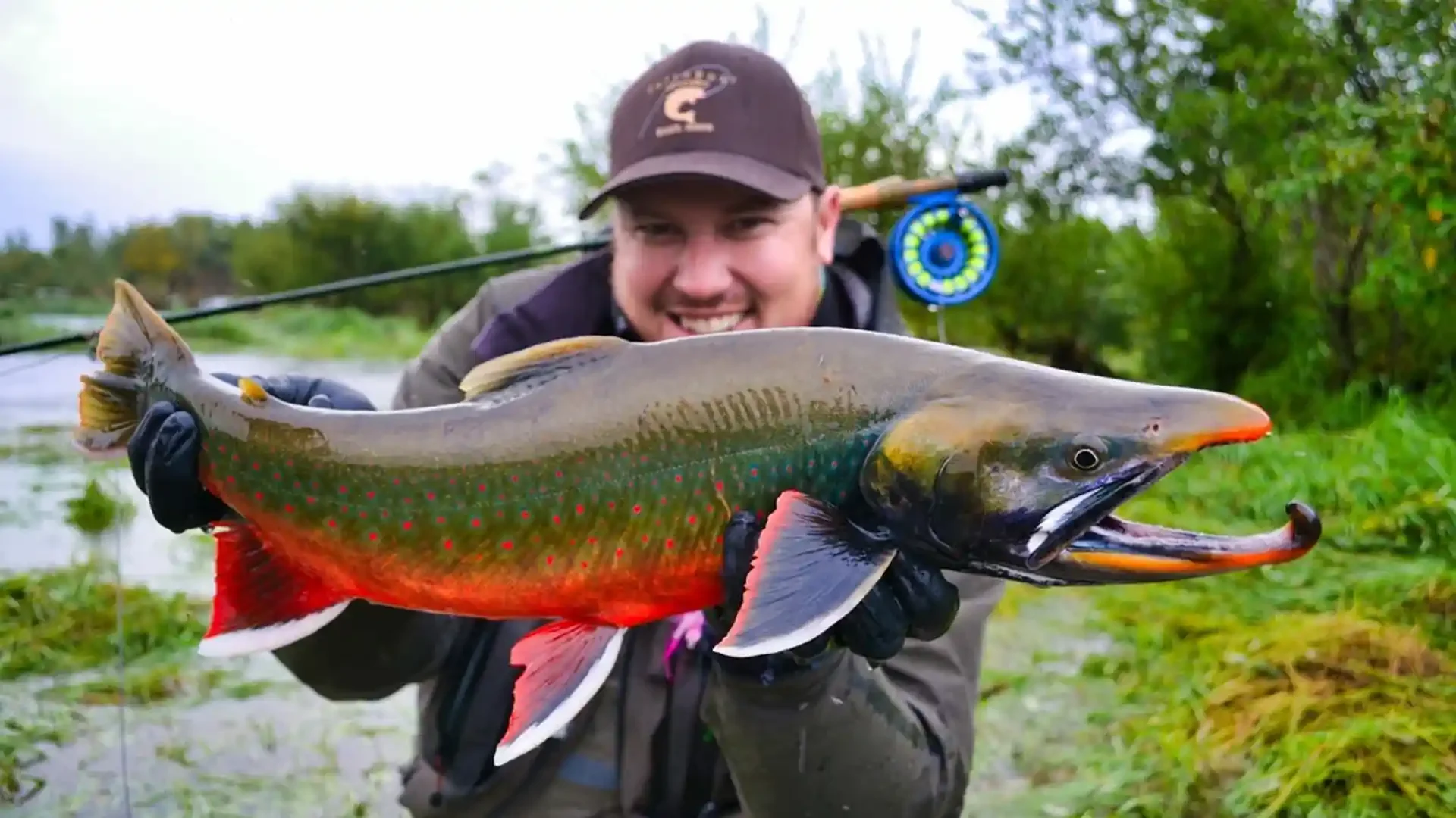 Smiling angler holding a vibrant spawning Arctic Char with a prominent kype on a fly fishing trip with Dave Duncan & Sons in Alaska.