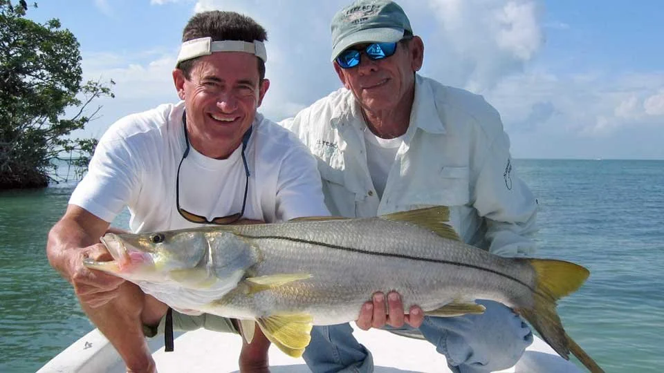 Angler and El Pescador Lodge guide on the bow of a boat displaying a large snook caught on the flats of Ambergris Caye, Belize.