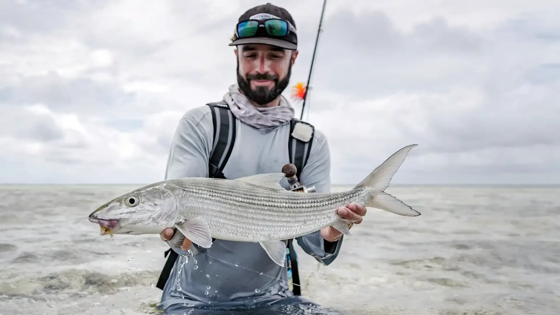 angler with hat sunglasses and backpack standing in waters of alphonse island holding large bonefish