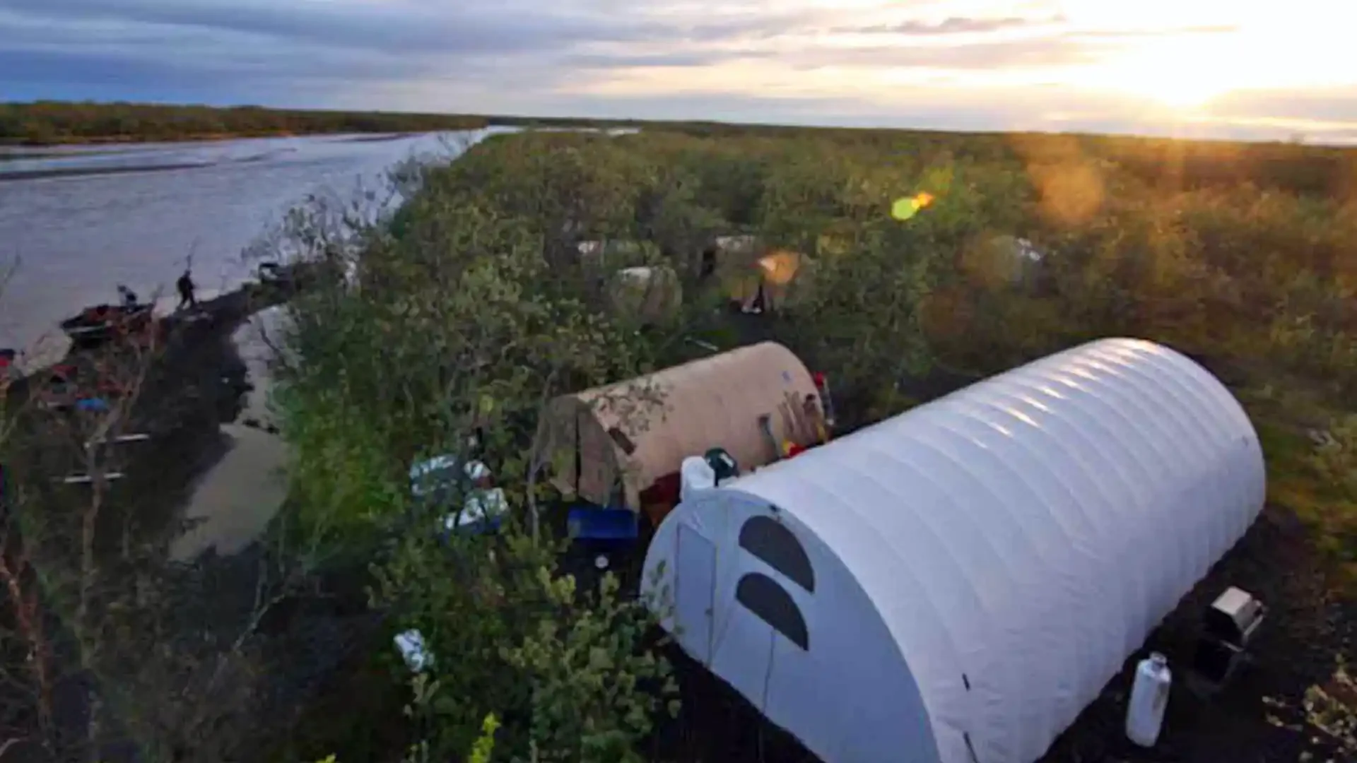 Alaskan fly fishing camp by Dave Duncan & Sons on a wide freestone river at sunset, with tents and boats on the bank.