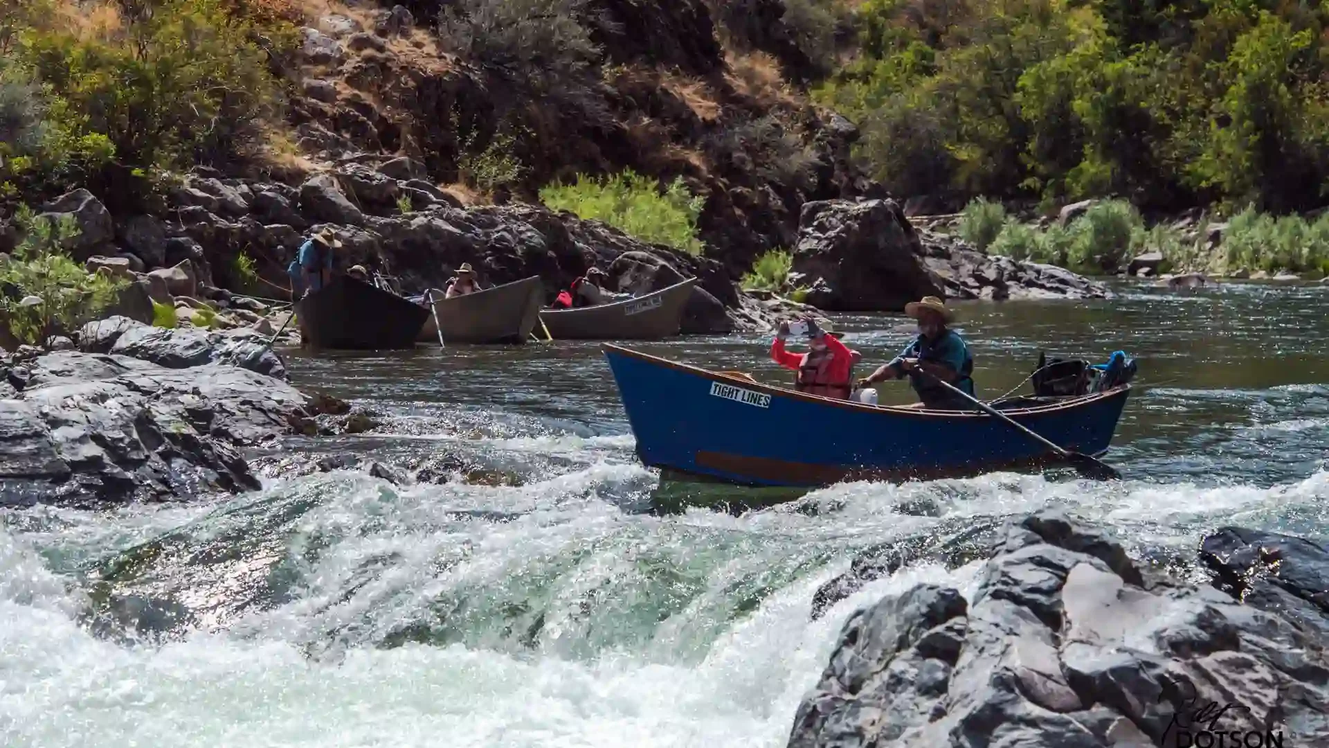 Drift boat navigating rapids on the Middle Fork of the Salmon River with other boats in the background.