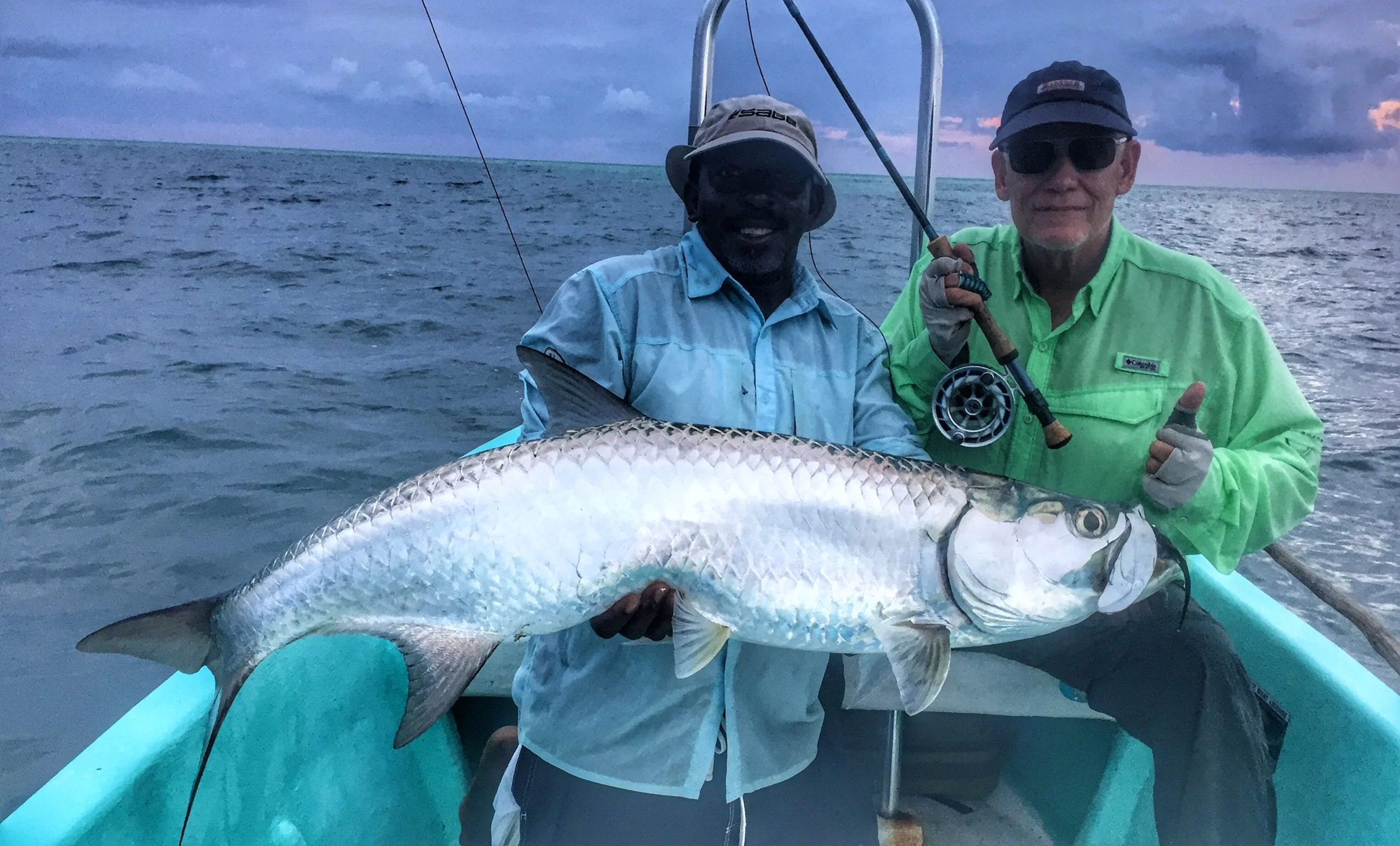 Two happy anglers in a boat holding a large tarpon caught fly fishing near Belize River Lodge, Belize.