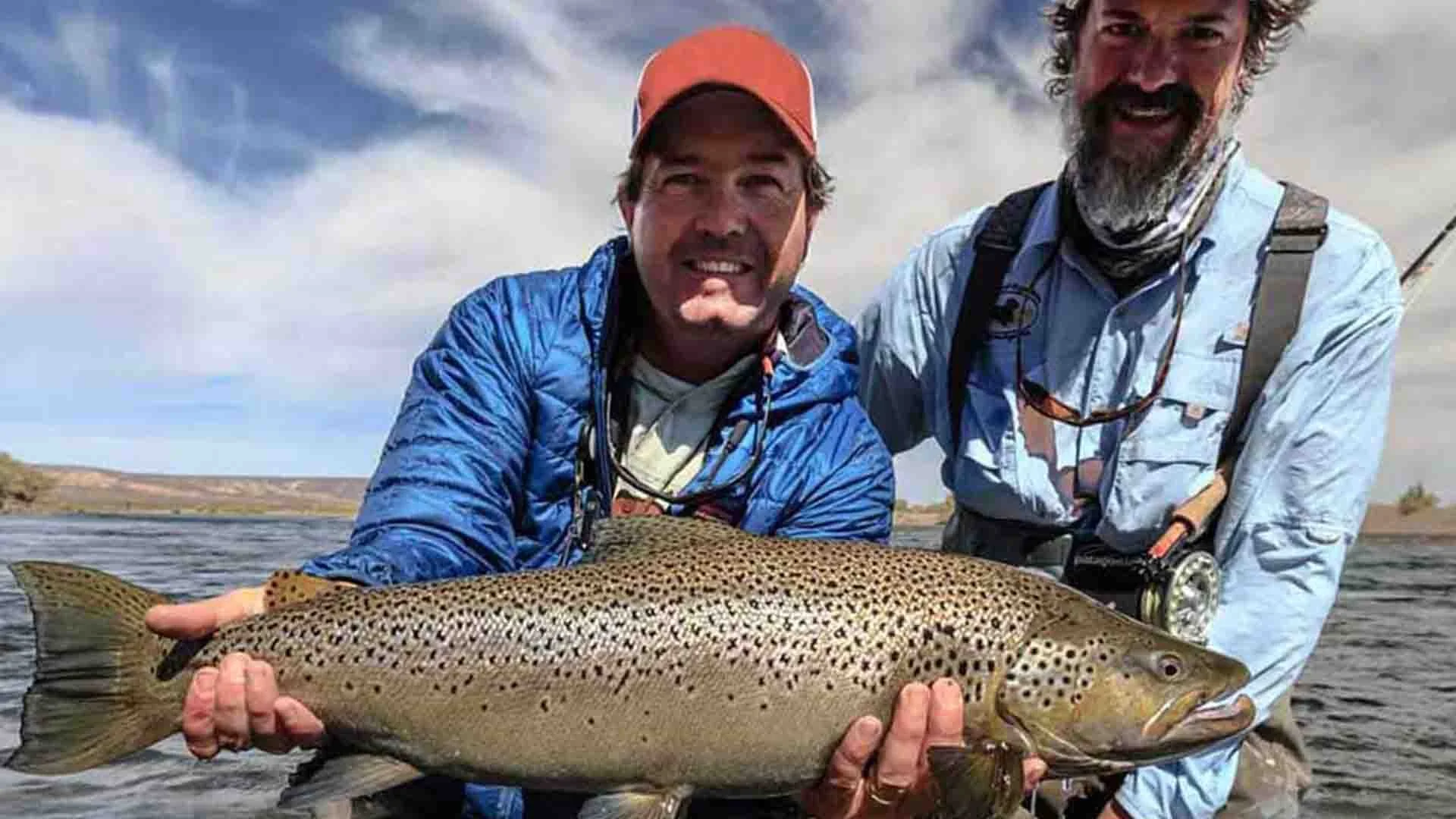 “Angler and guide holding a massive brown trout on the Limay River in Patagonia during a Three Rivers fishing trip with Chocolate Lab Expeditions.”