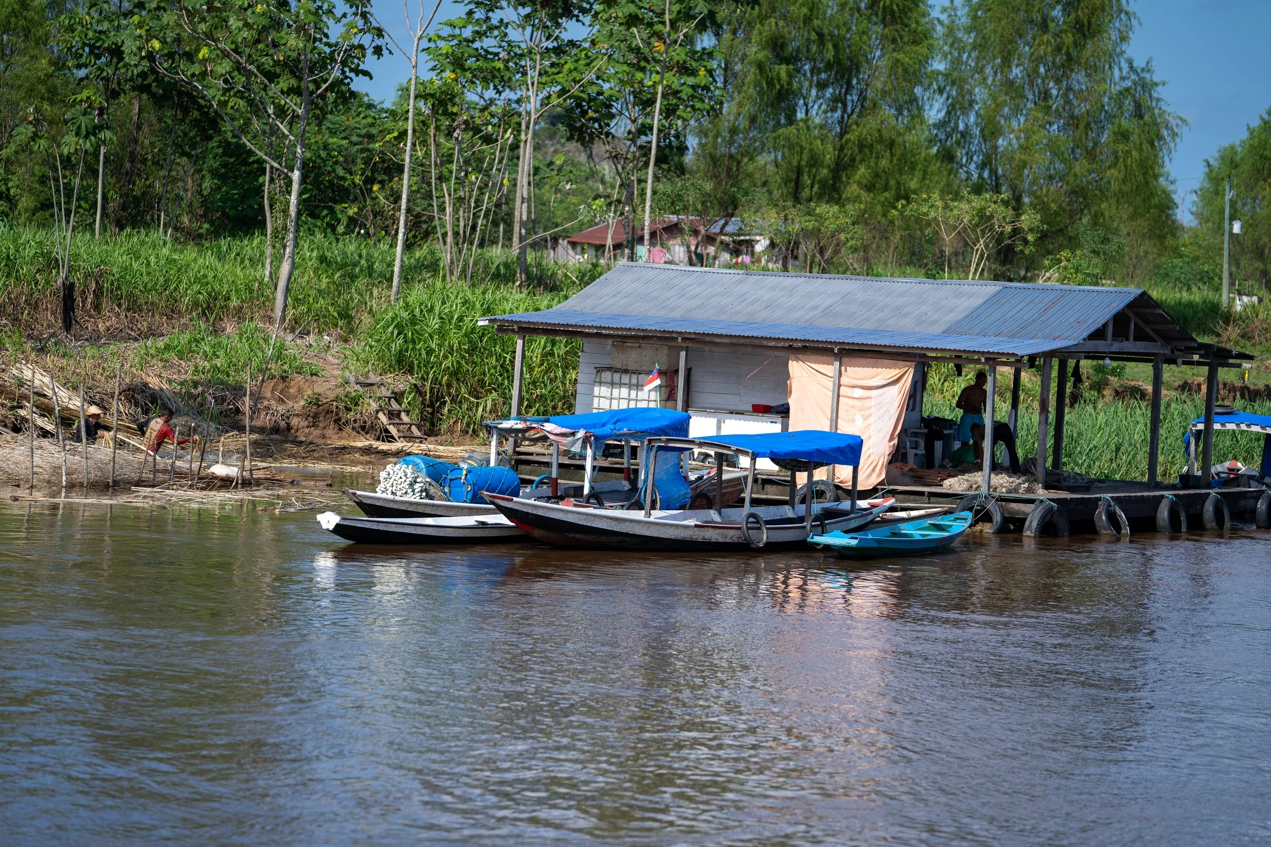 Boats docked beside a wooden riverside hut with a tin roof and surrounding trees