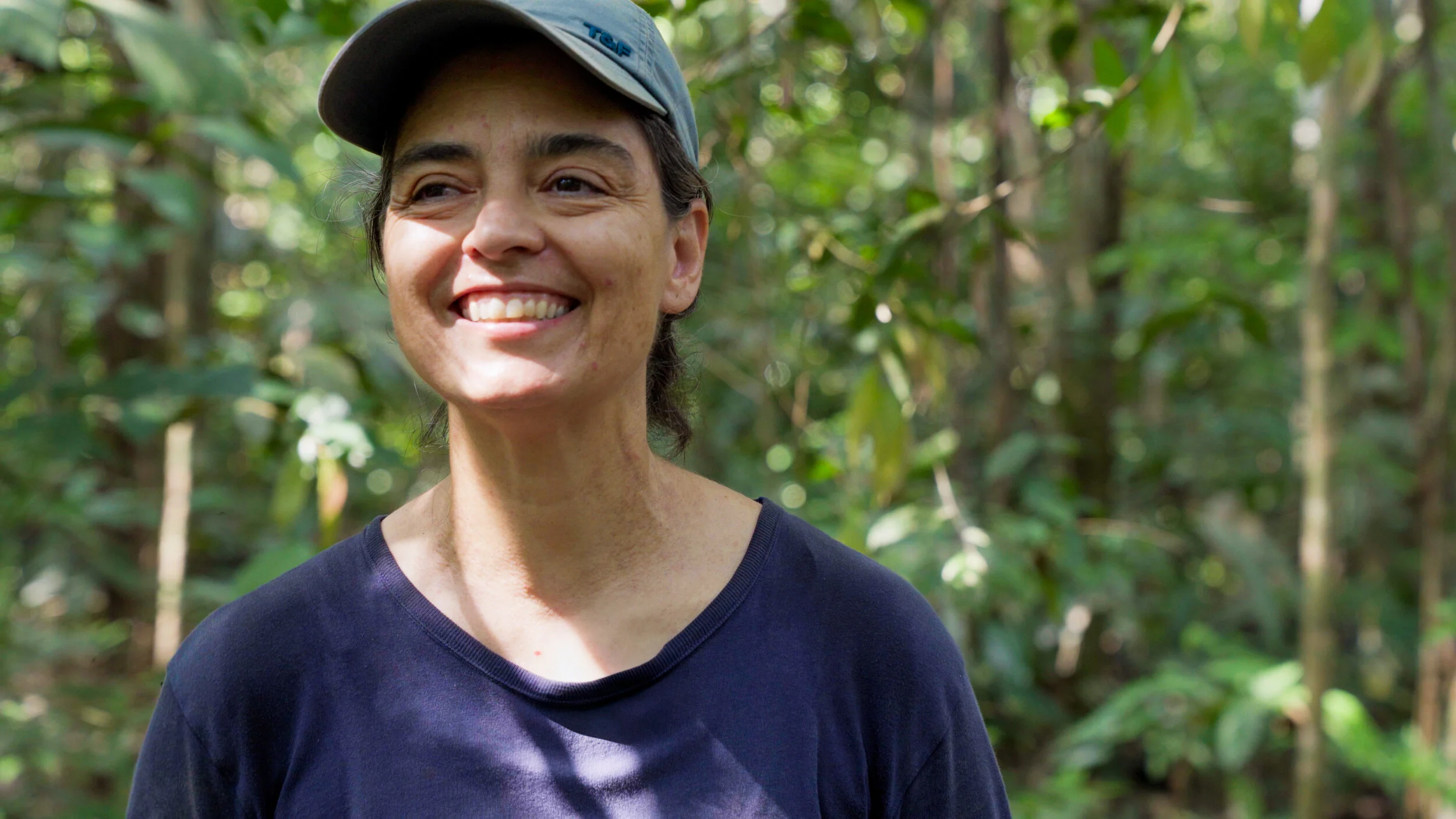 Smiling person wearing a cap in a forested area