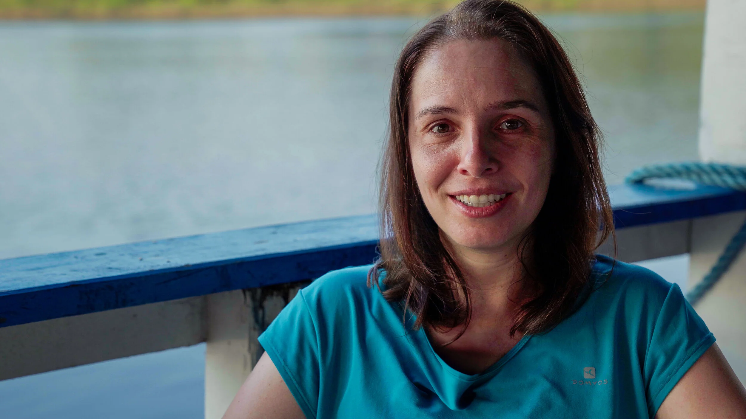 Woman in a blue shirt smiling on a boat with a waterfront background.
