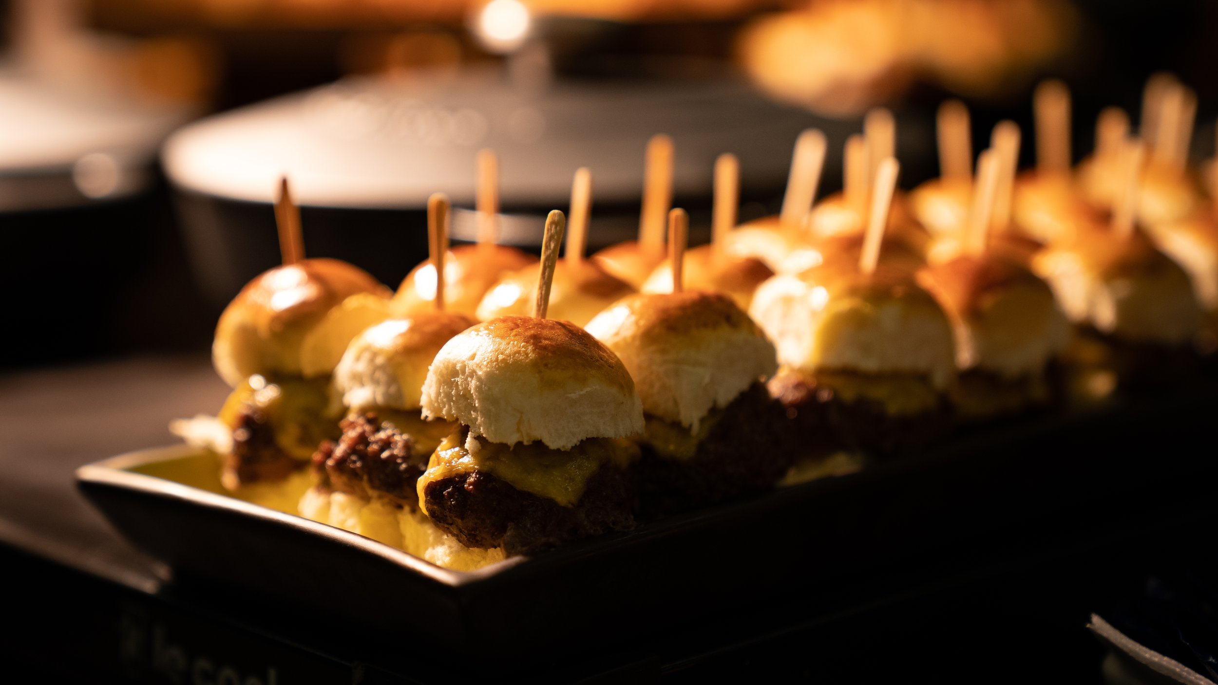 Mini cheeseburger sliders with skewers on a serving tray.