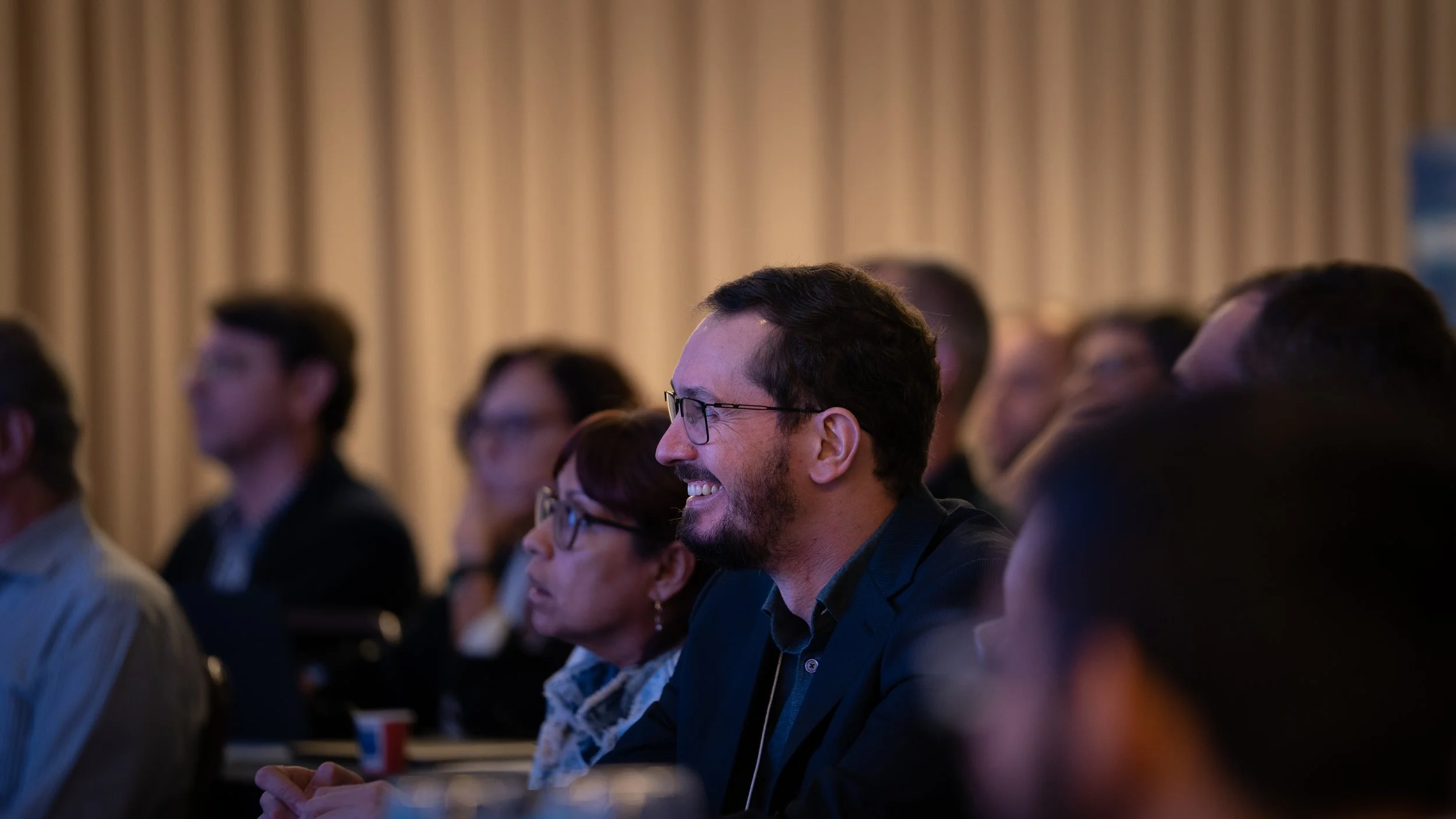 Audience members attentively watching a presentation, with one man smiling.