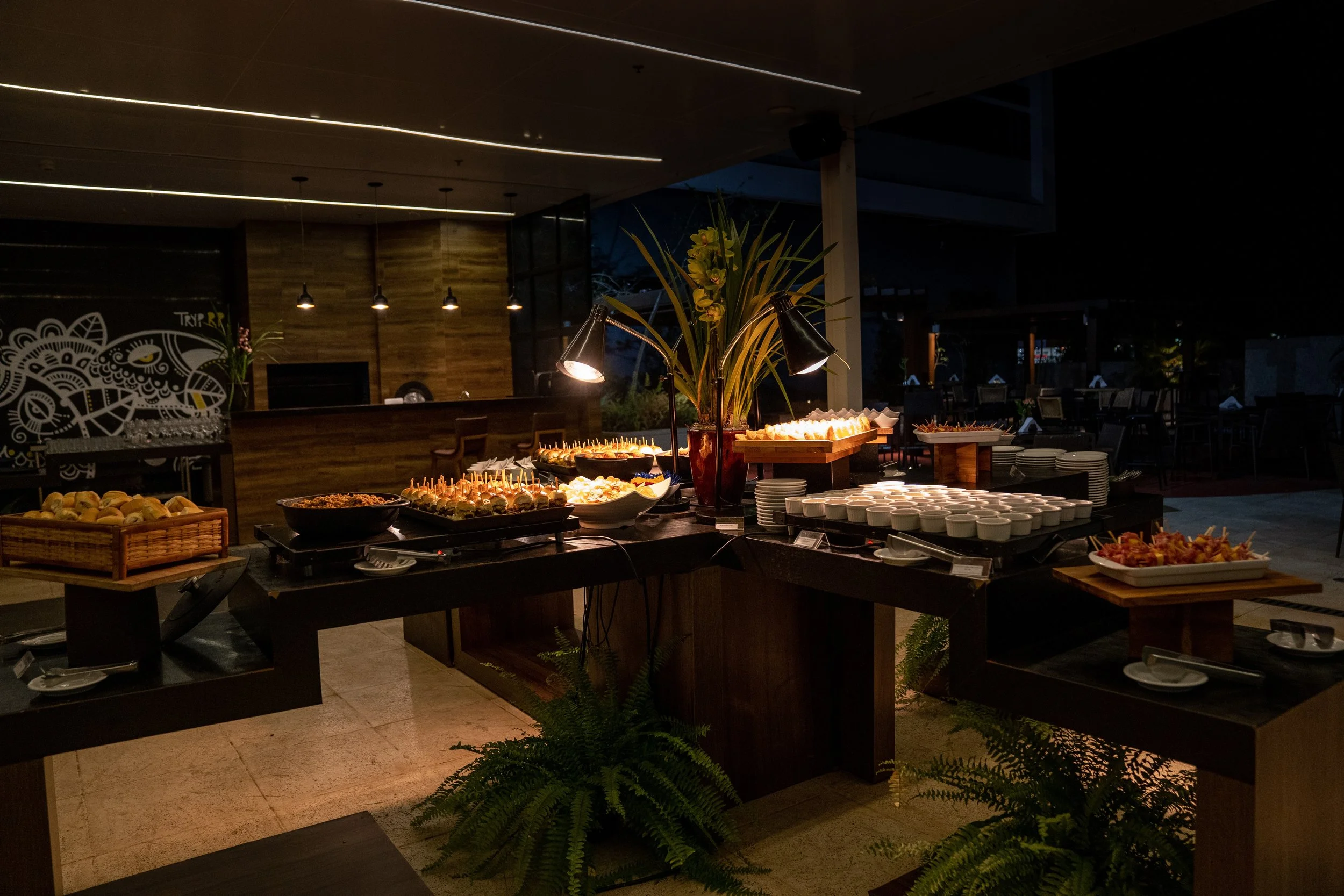 Buffet table with various foods and desserts, including pastries, skewers, and small bowls, in a dimly lit restaurant setting.