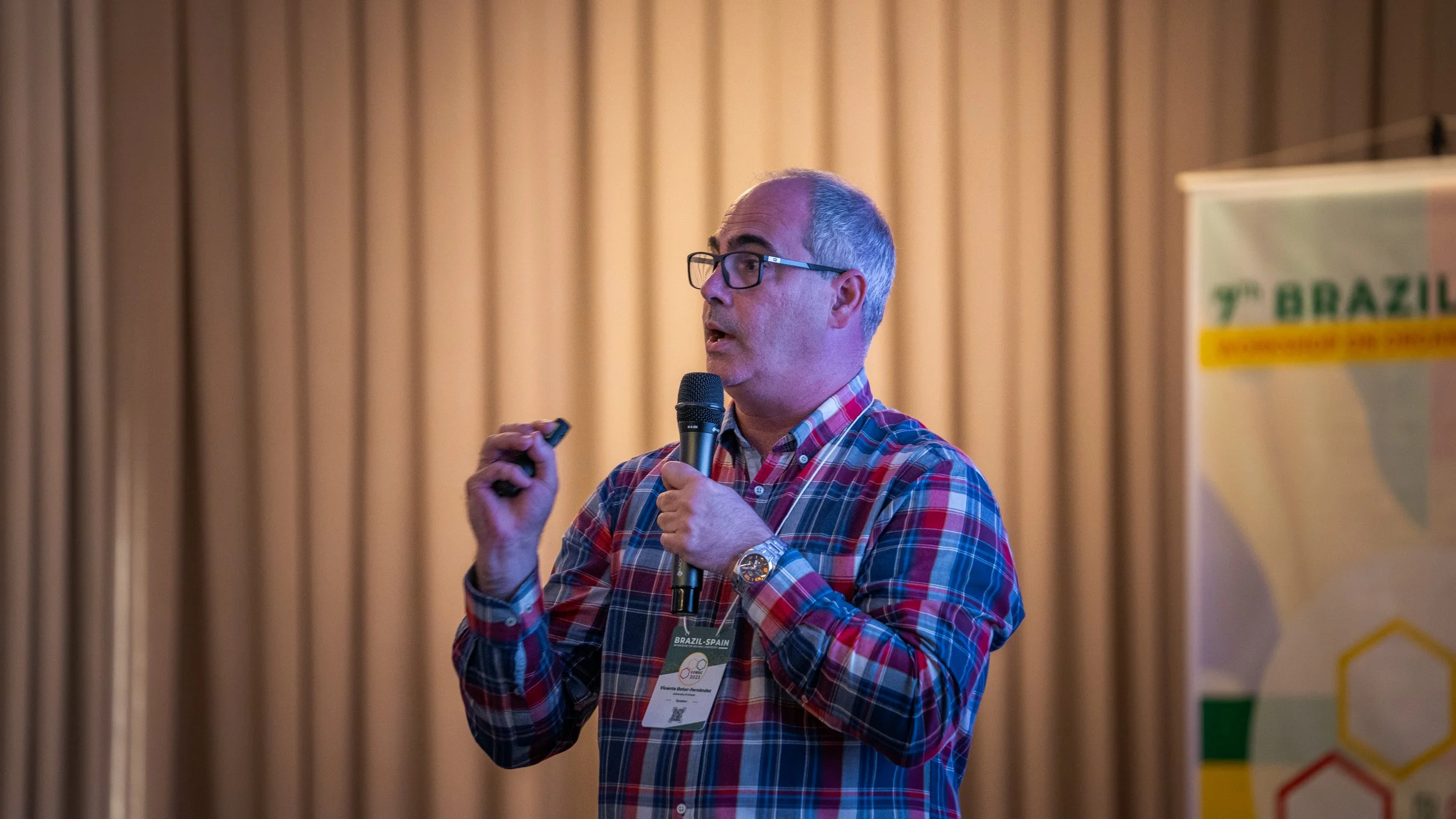Man in plaid shirt speaking into a microphone at a conference
