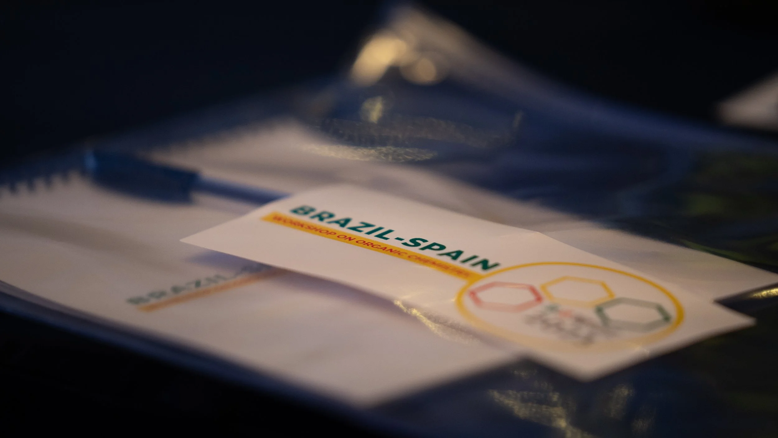 Badge labeled 'Brazil-Spain Workshop on Organic Chemistry' on table with pen.