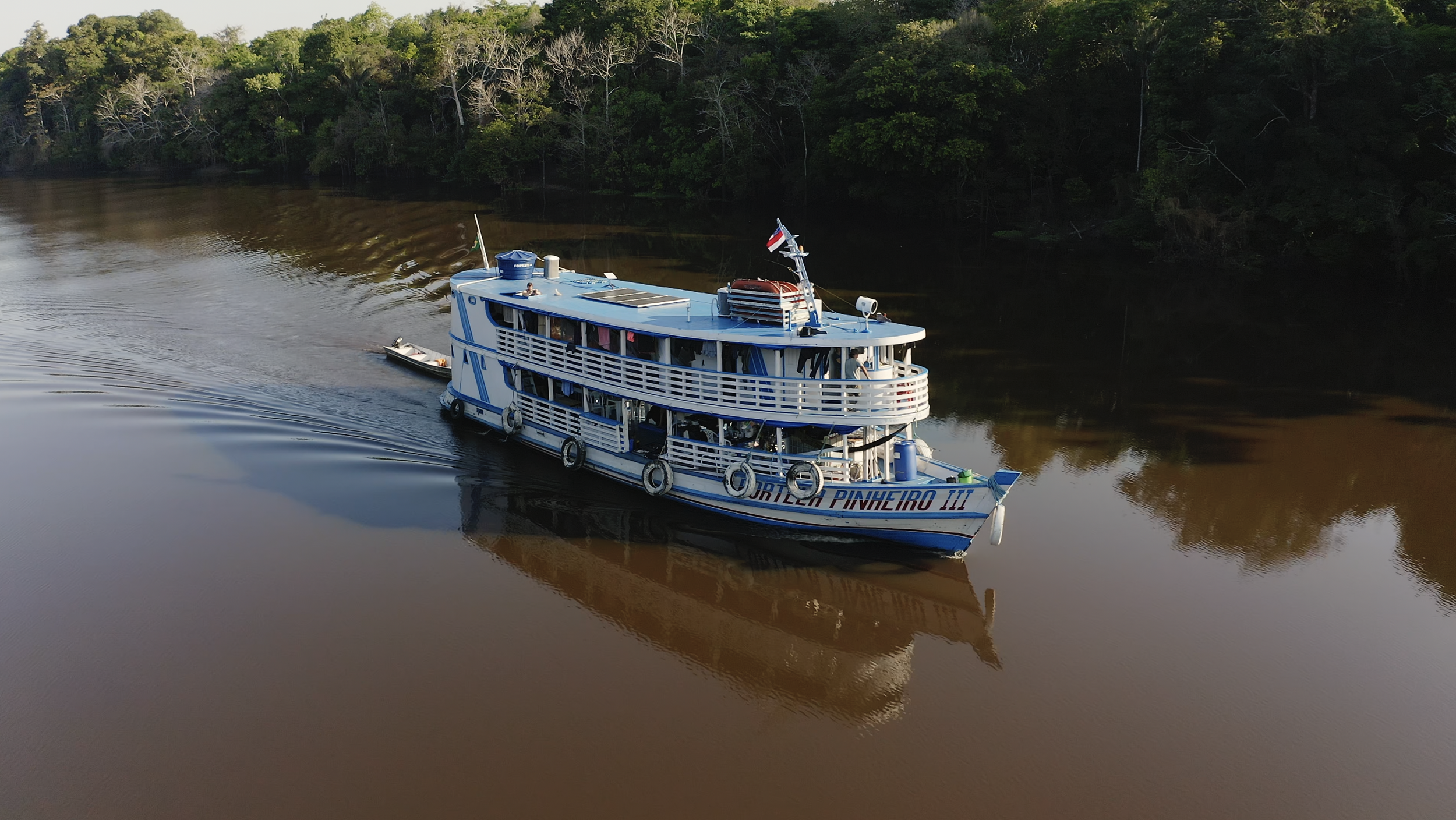 Riverboat on a calm river with forested banks in the amazon rainforest on the rio purus
