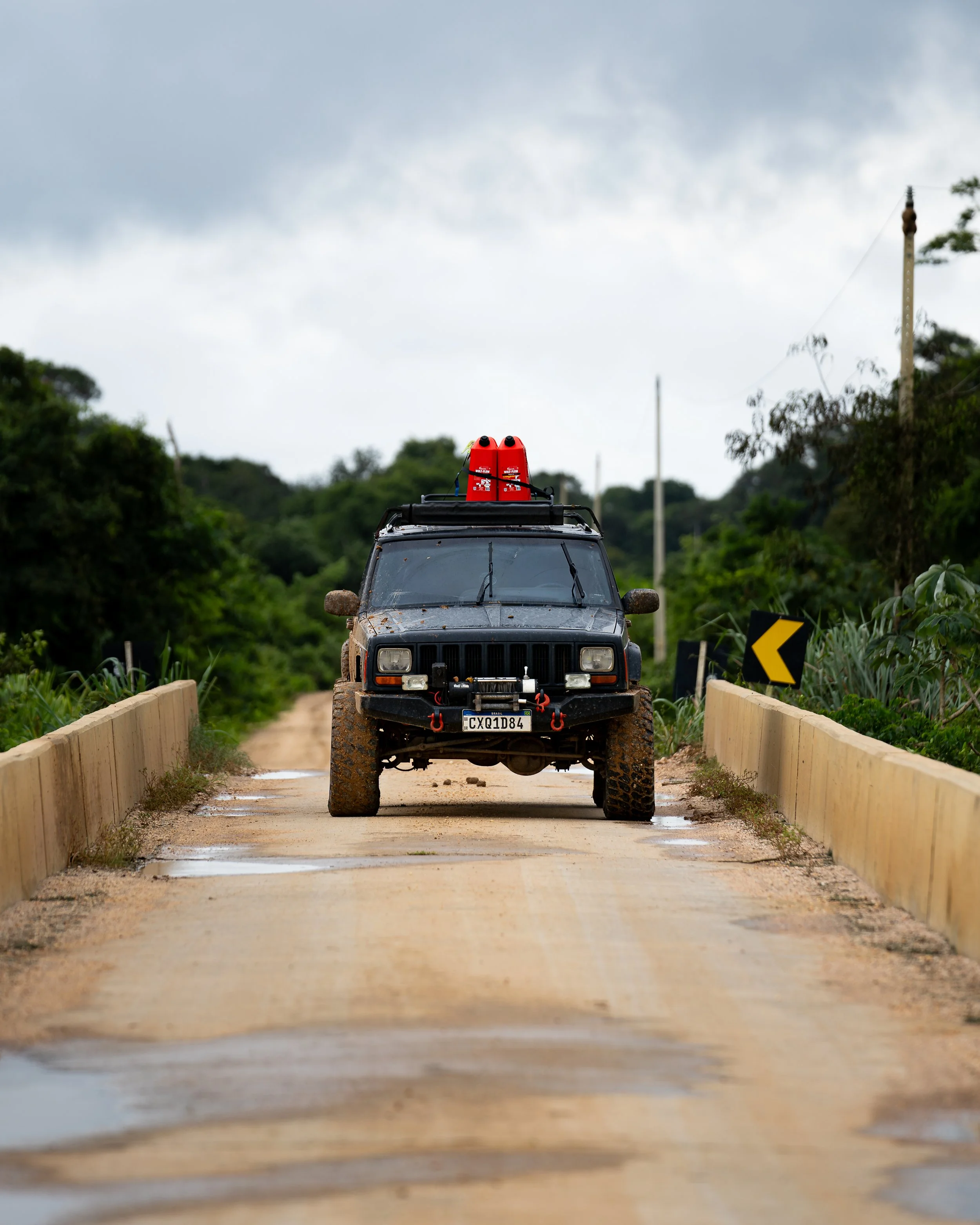 A muddy off-road vehicle, jeep cherokee 1998 with red gas cans on the roof driving on a dirt road surrounded by greenery on the transpantaneira in pantanal brazil