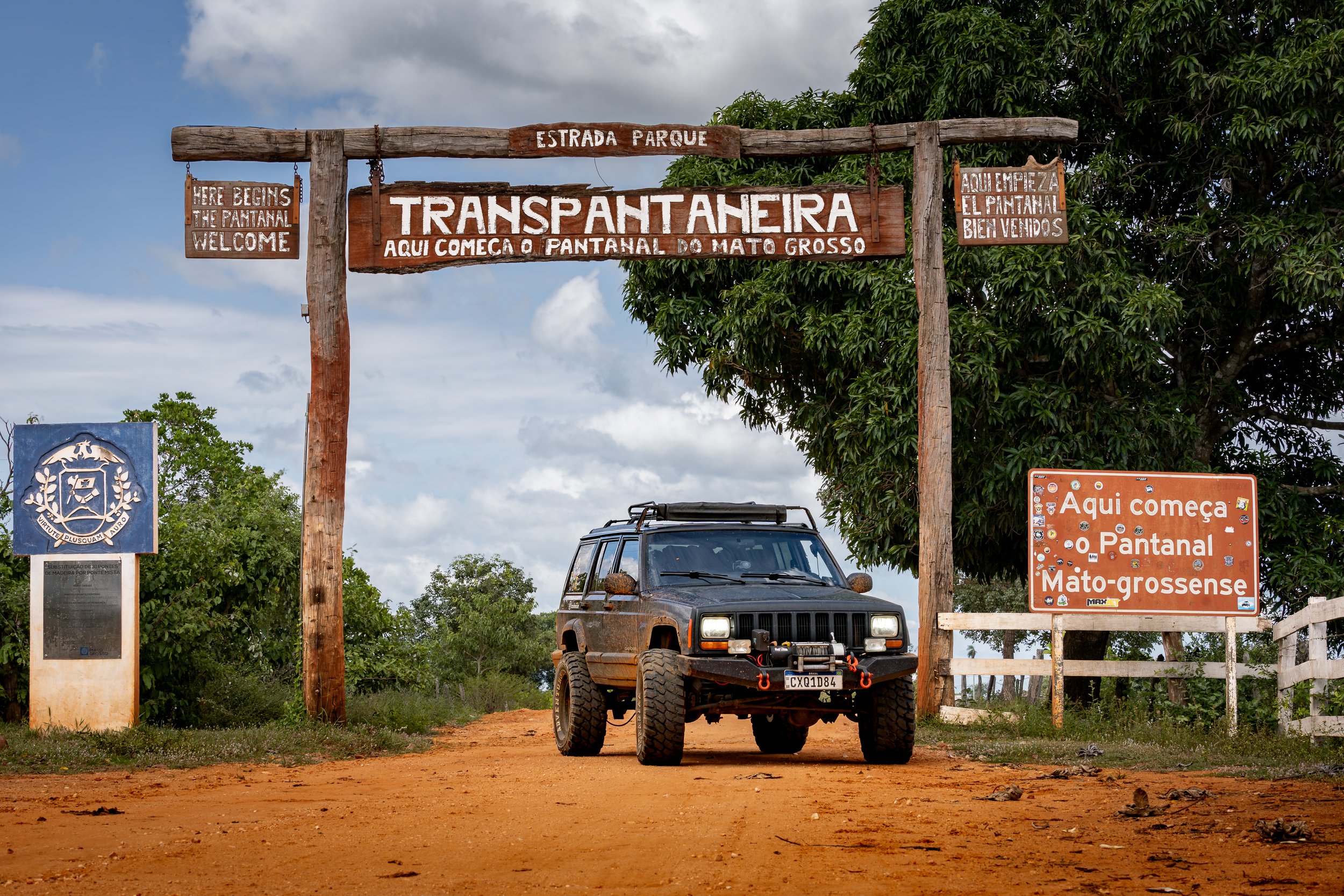 Off-road vehicle, jeep cherokee 1998 on dusty road under wooden sign marking the entrance to Transpantaneira Highway in Mato Grosso, Brazil.