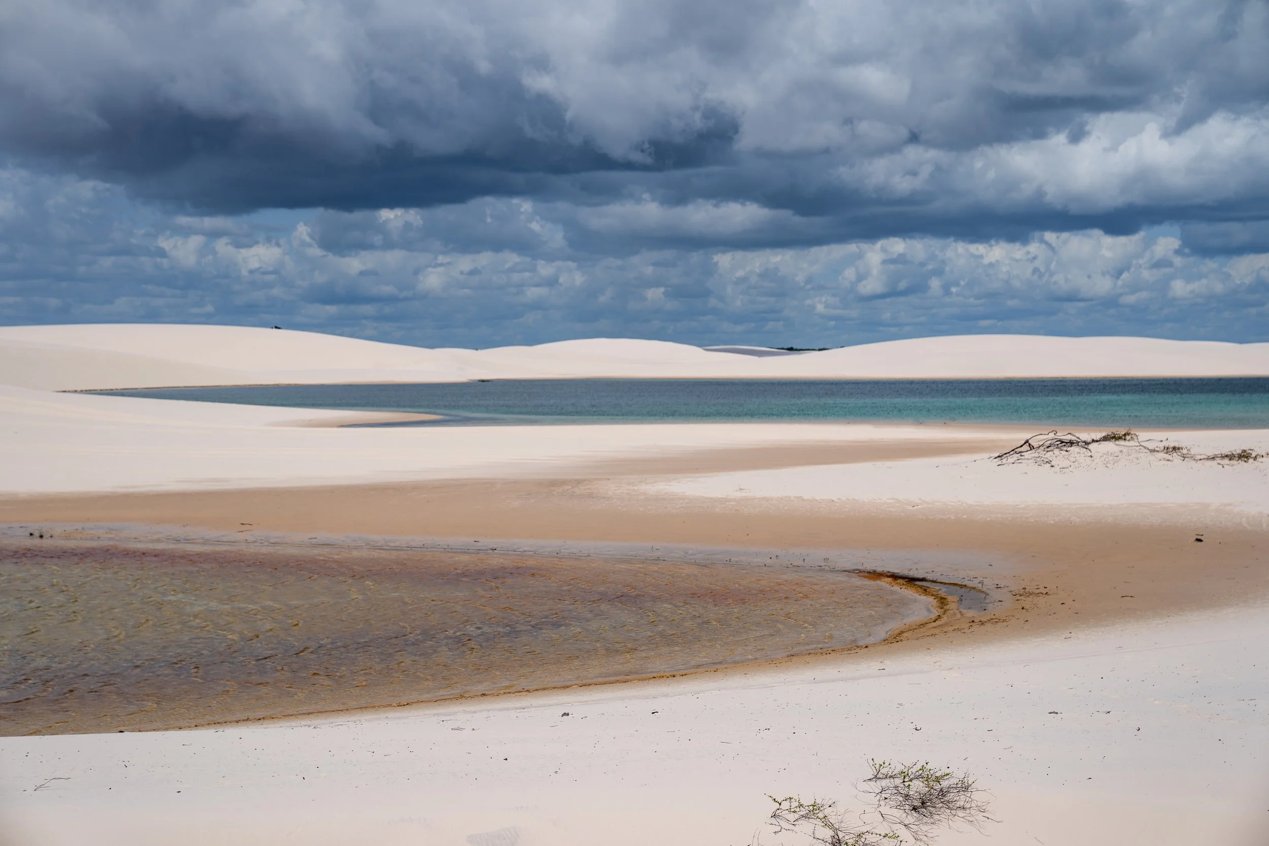 Sand dunes with a small body of water, under a cloudy sky.