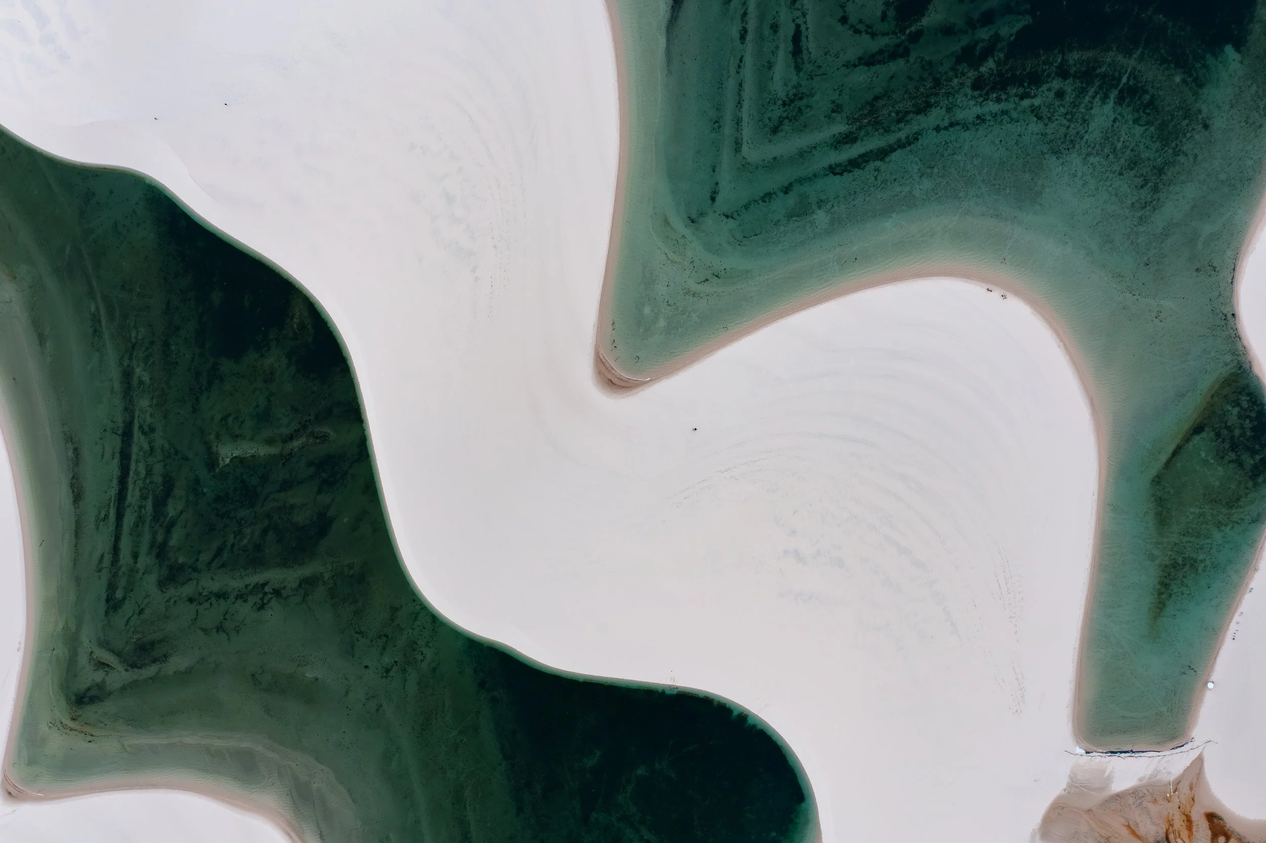 Aerial view of a beach with white sand and green waters surrounded by rocky formations.