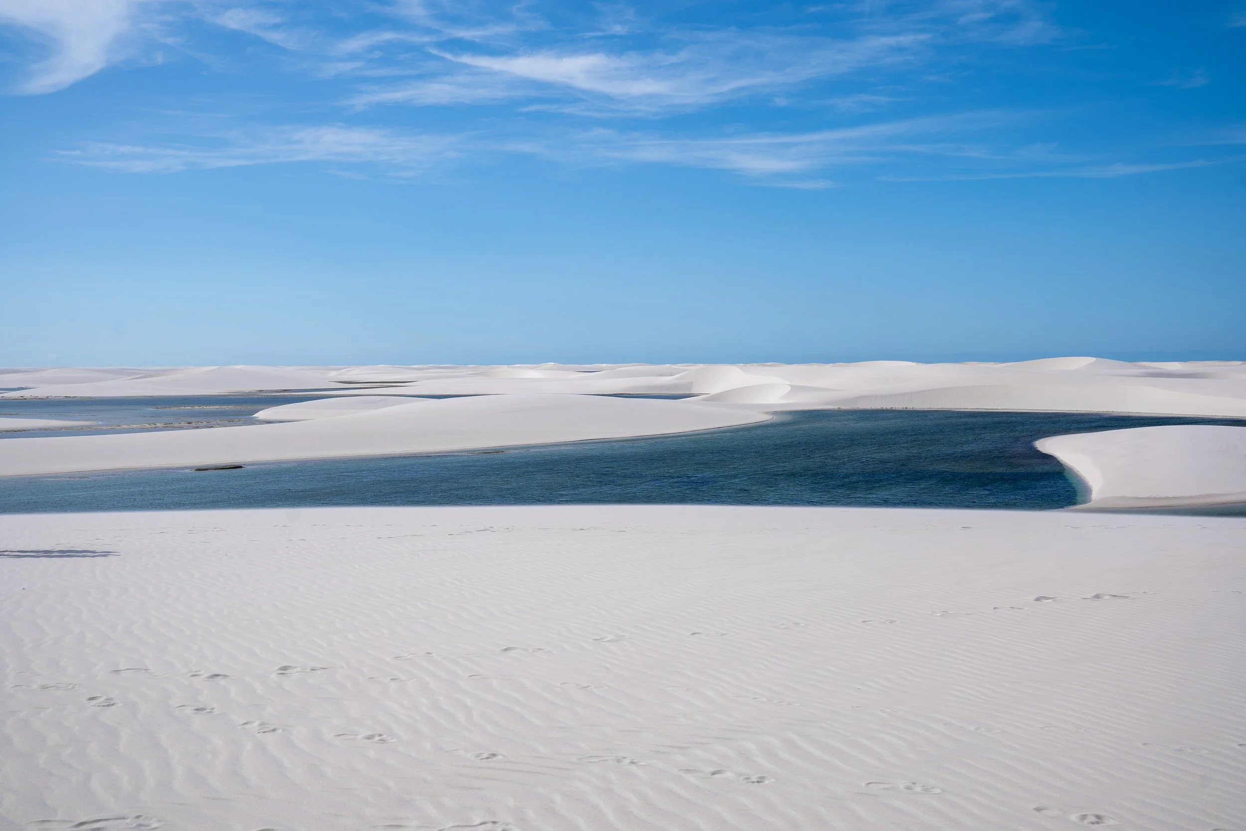 White sand dunes with winding blue water channels and a bright blue sky with wispy clouds.