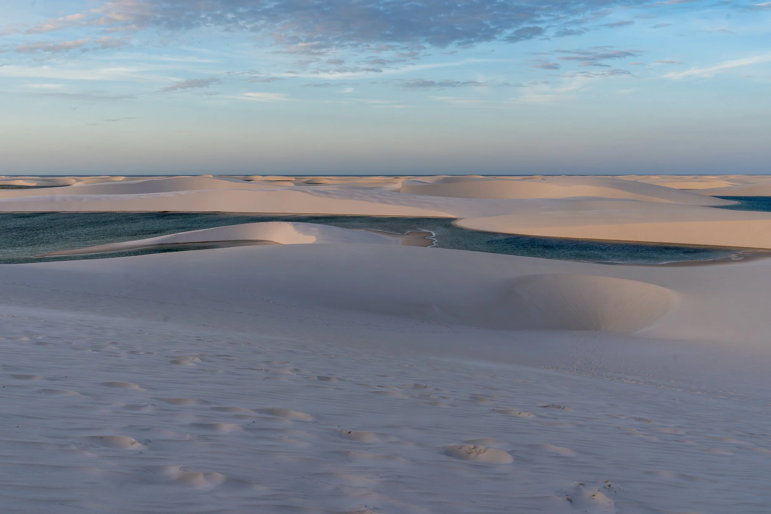 White sand dunes with patches of water under a partly cloudy sky.