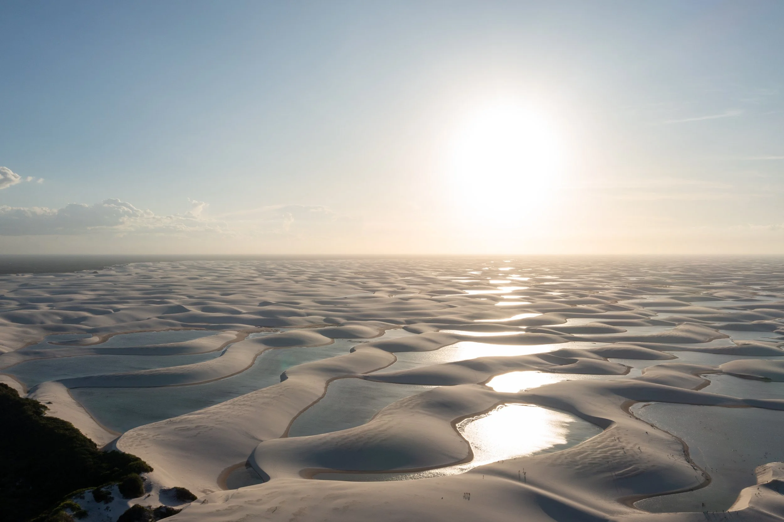 Landscape of white salt flats with reflecting shallow pools under a bright sun and a partly cloudy sky.