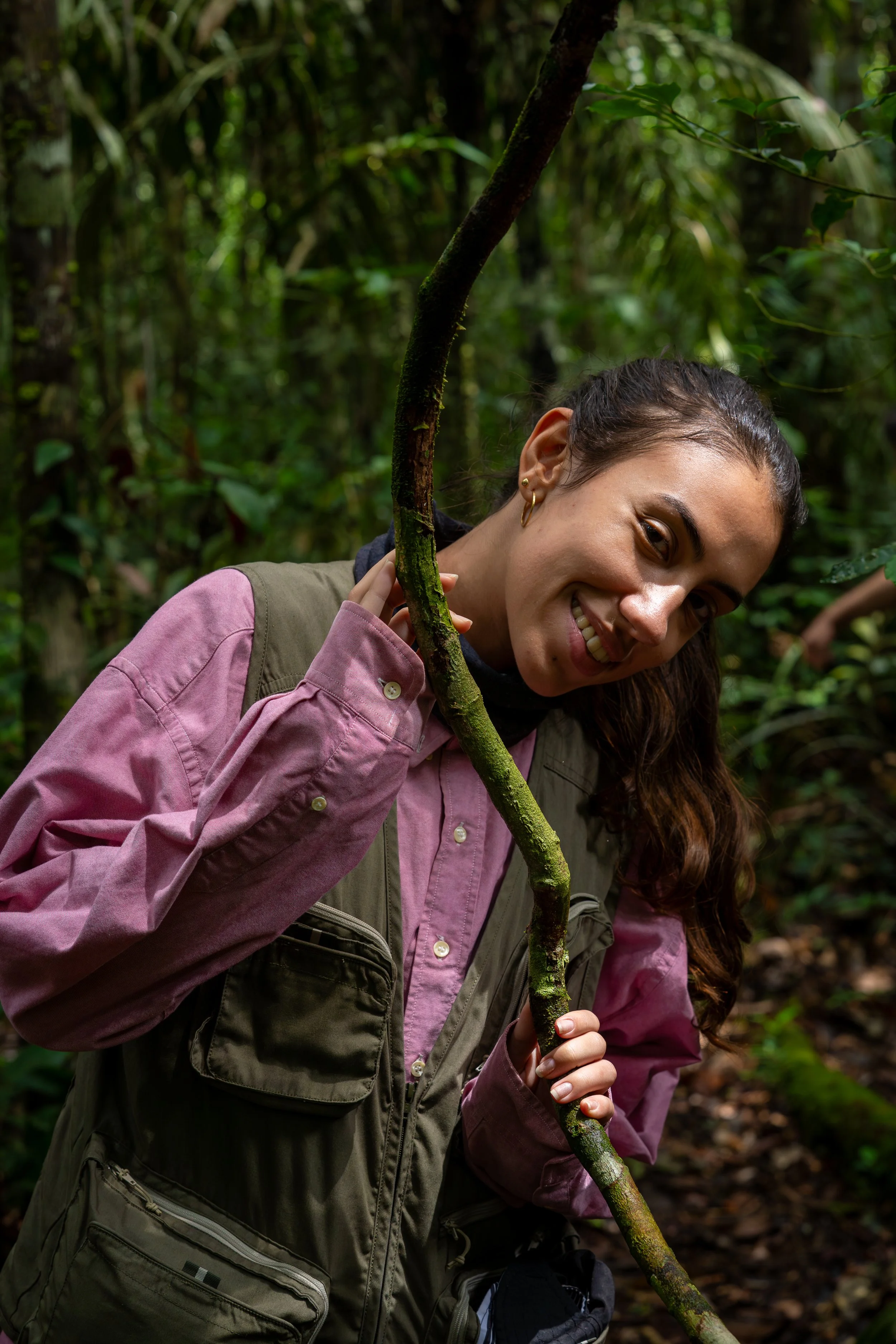 Julia A. Pinna in outdoor clothing smiling and holding a vine in a forested area.