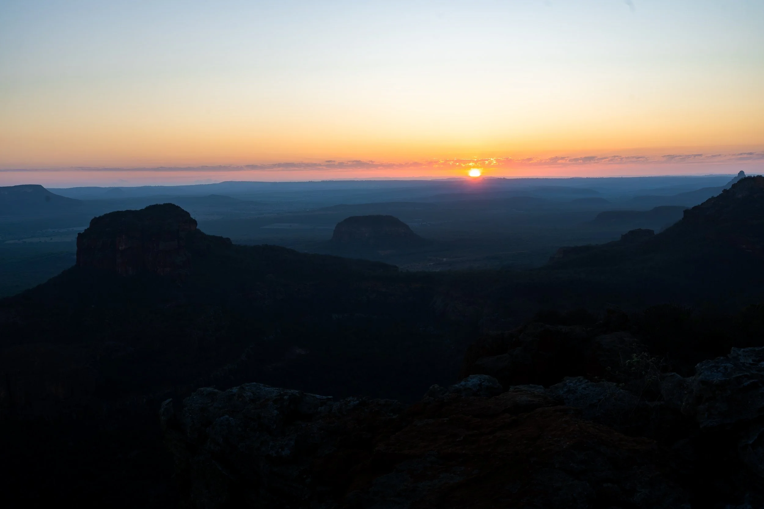 Sunset over a mountainous landscape with layered ridges and a partly cloudy sky.