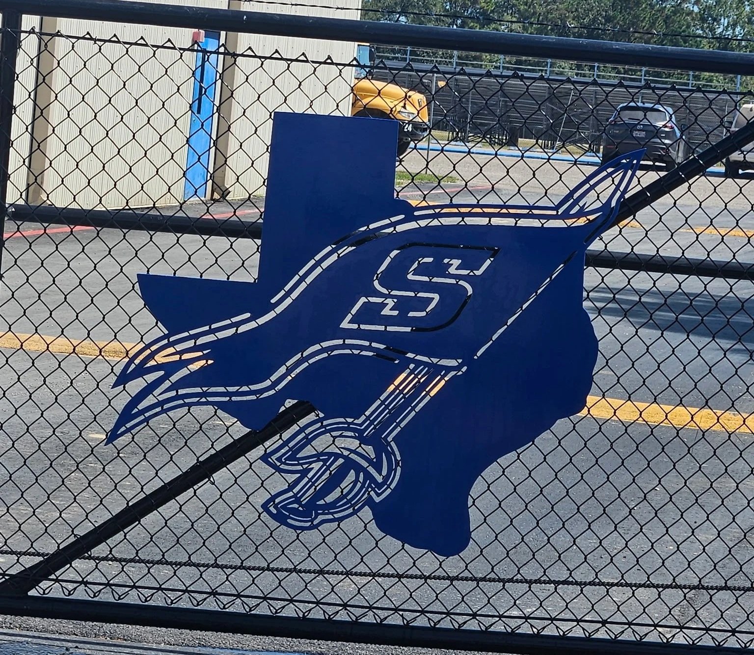 Blue metal sign on a chain-link fence depicting a crossed-out motor scooter with a road behind it.
