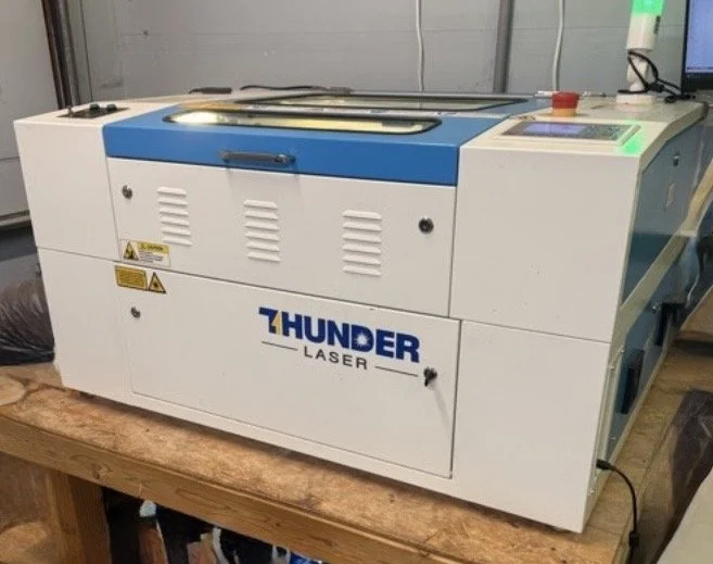 A Thunder Laser engraving machine on a wooden workbench in a workshop.